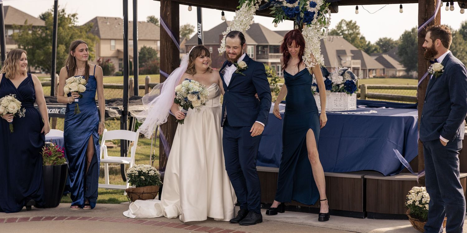 Outdoor wedding ceremony with bride in white gown and groom in navy suit, flanked by bridesmaids in blue dresses.