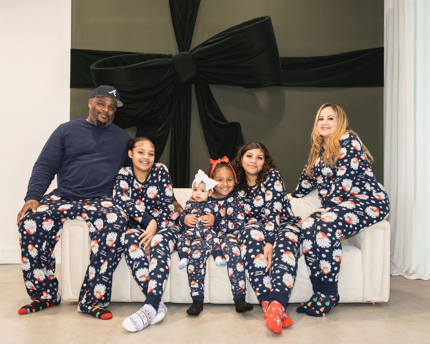 Family of six wearing matching navy floral pajamas poses together on a white couch for a holiday photo.
