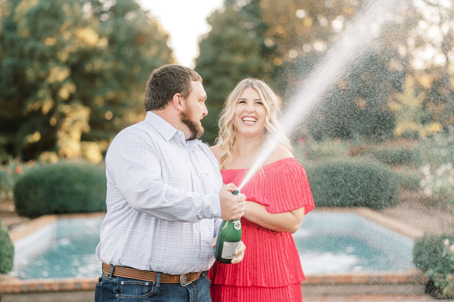 A couple celebrates with champagne in a garden setting with a fountain and golden sunset light in the background.  Wedding Photographer