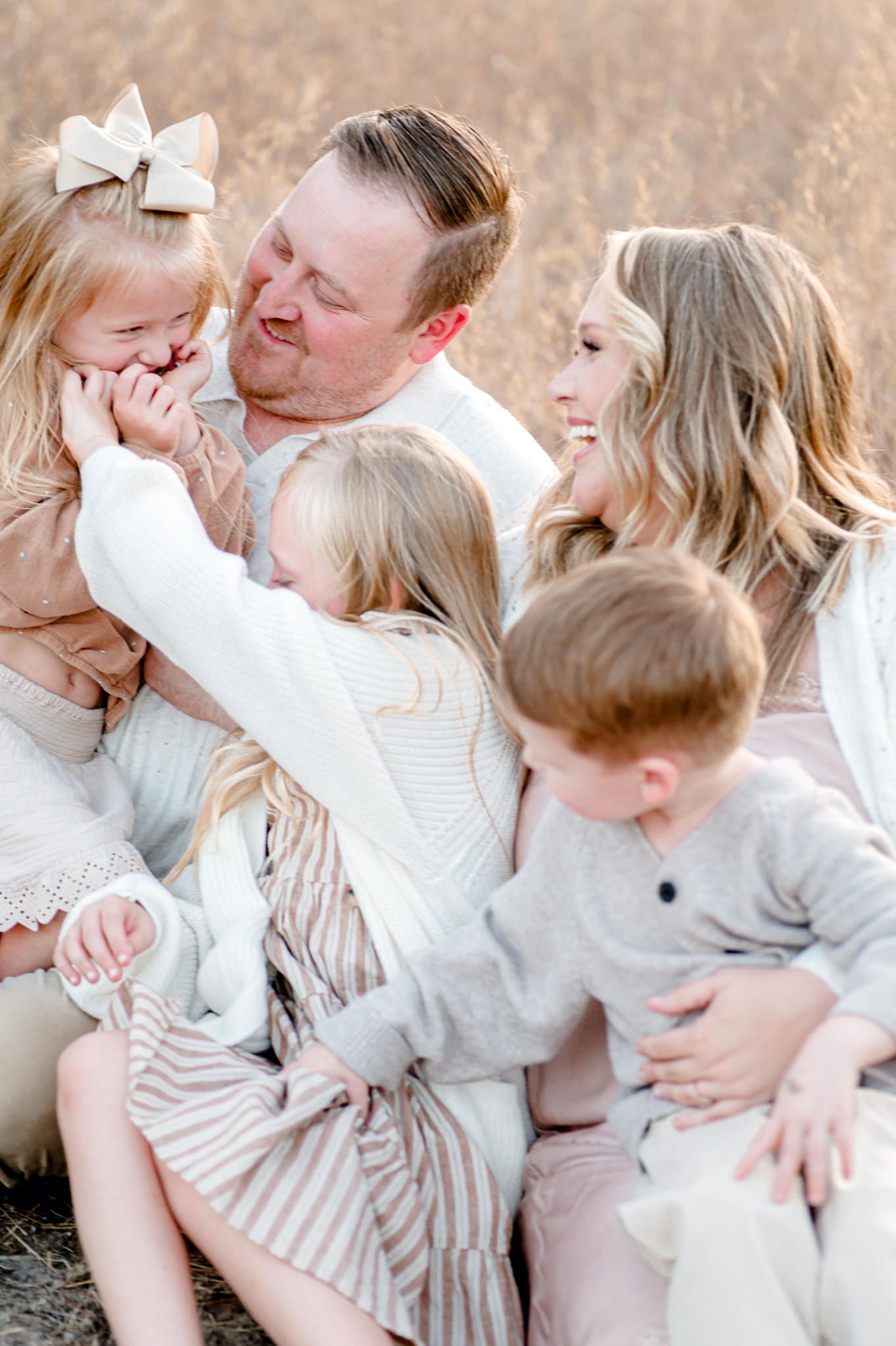 A family wearing white and beige clothing poses together outdoors in a series of candid affectionate moments.  Wedding Photographer tyler tx