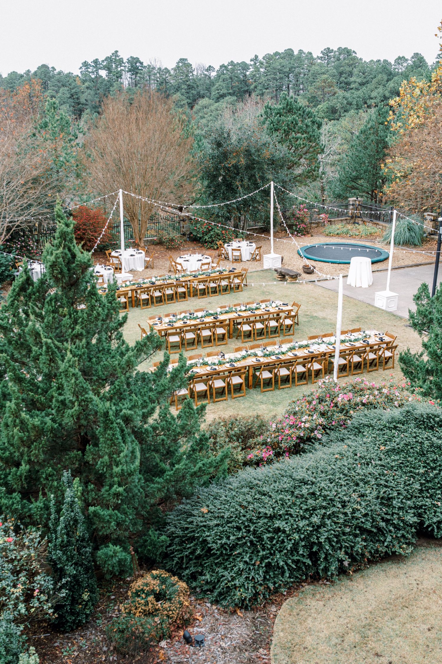 Outdoor wedding venue setup with rows of wooden chairs arranged on a hillside surrounded by evergreen trees and autumn foliage.