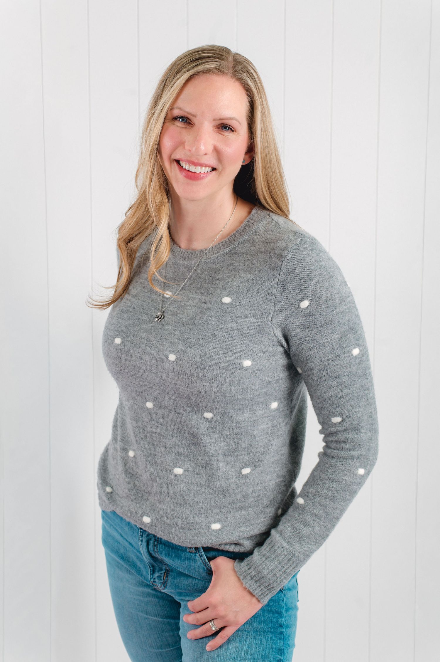 Person wearing a cozy gray sweater with white polka dots and blue jeans poses against a white background.