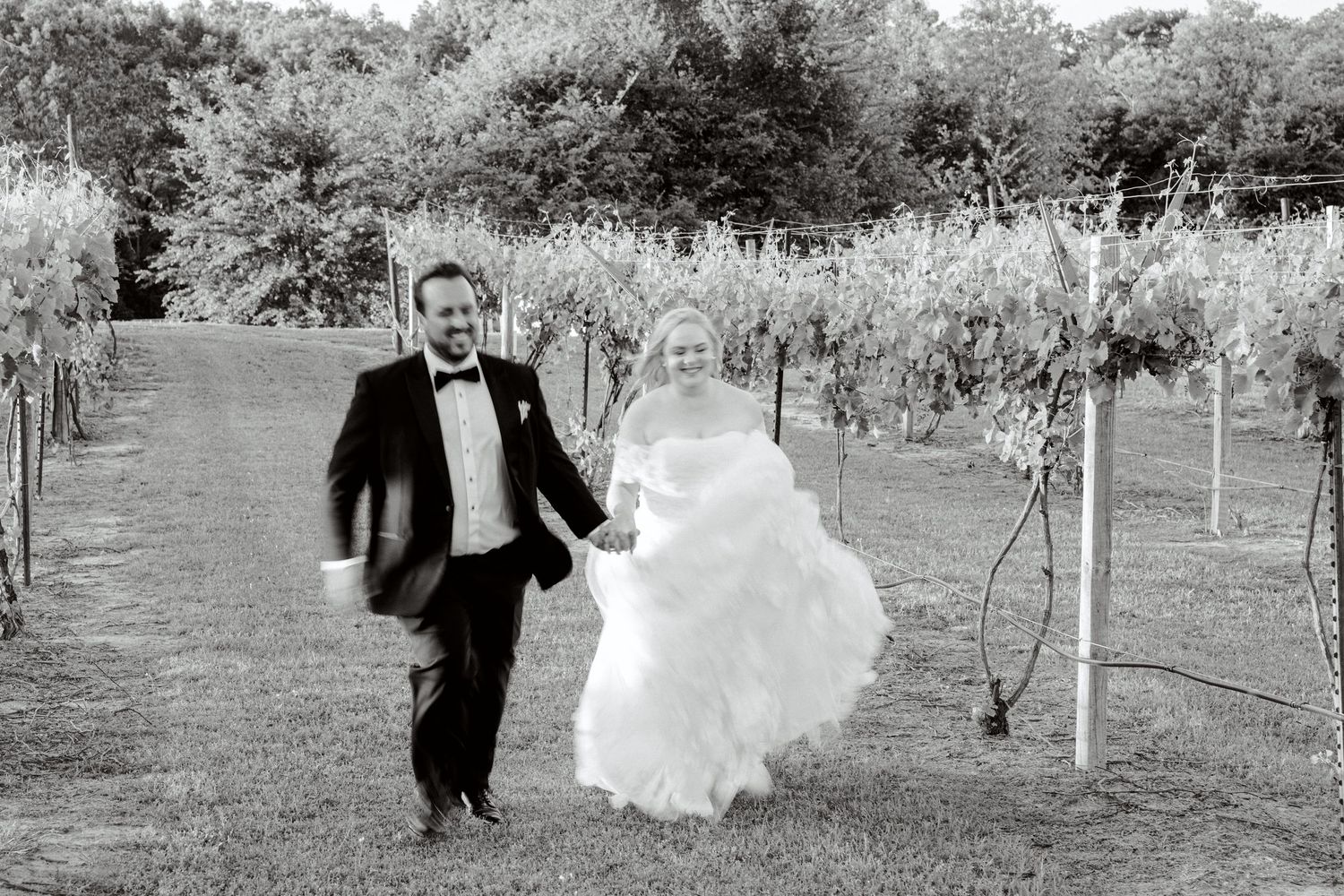 Newlywed couple walks through an orchard together on their wedding day, holding hands and smiling. Wedding Photographer tyler tx