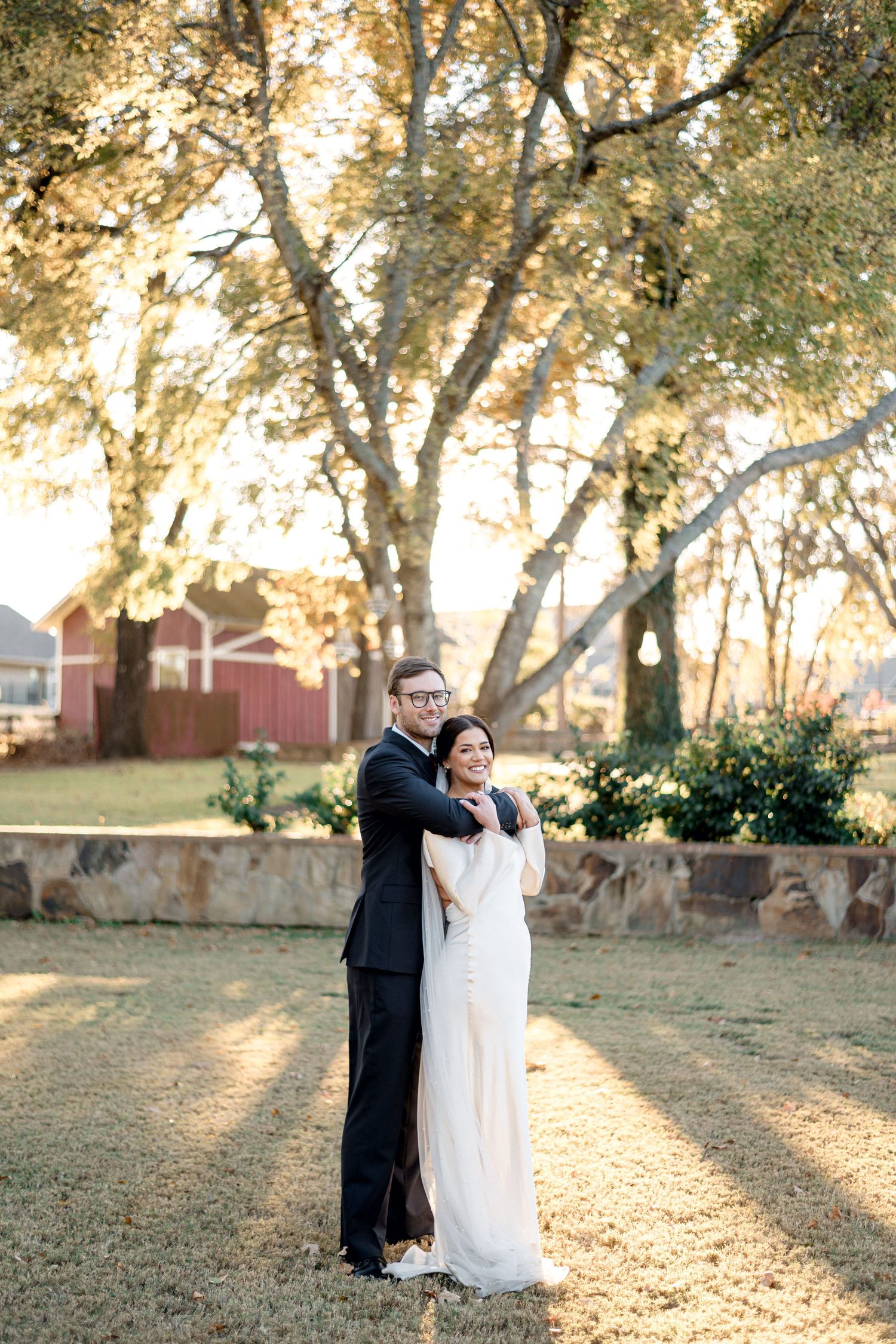 A couple shares a romantic moment during golden hour under autumn trees at an outdoor wedding venue.