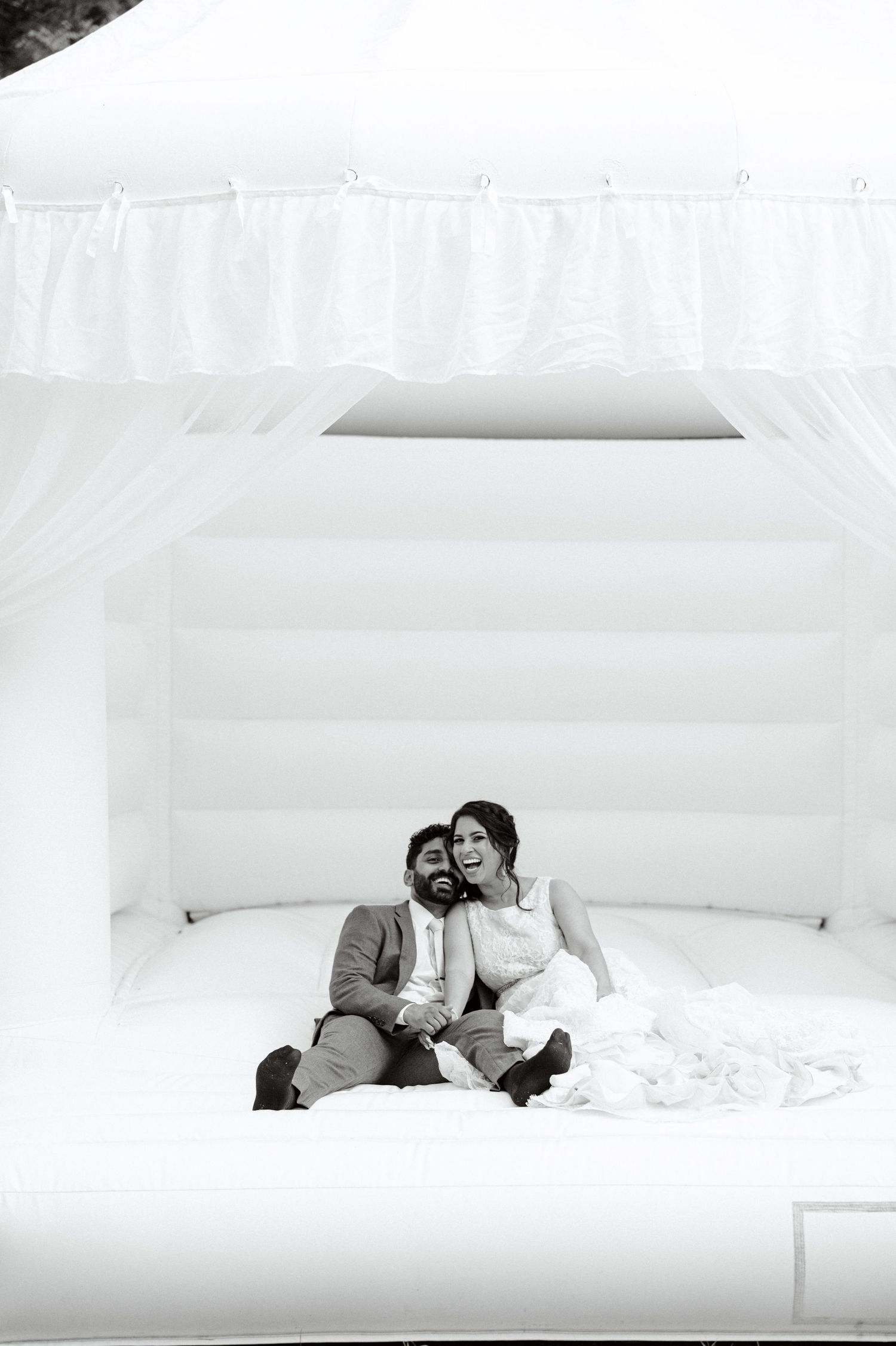 Black and white photo of a couple lounging intimately on a white bounce house.  Wedding Photographer tyler tx