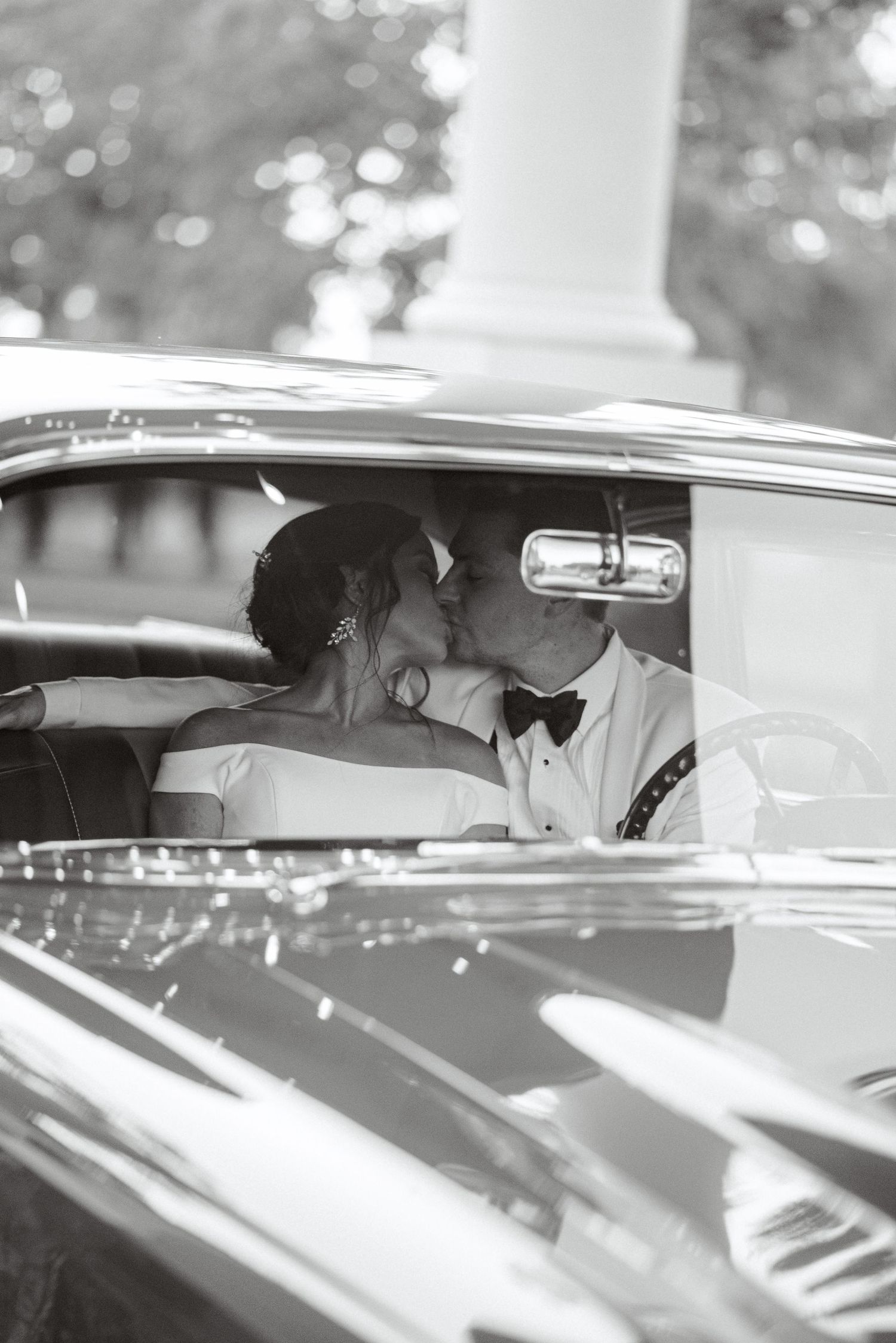 Classic black and white photo of newlyweds in vintage car after ceremony.