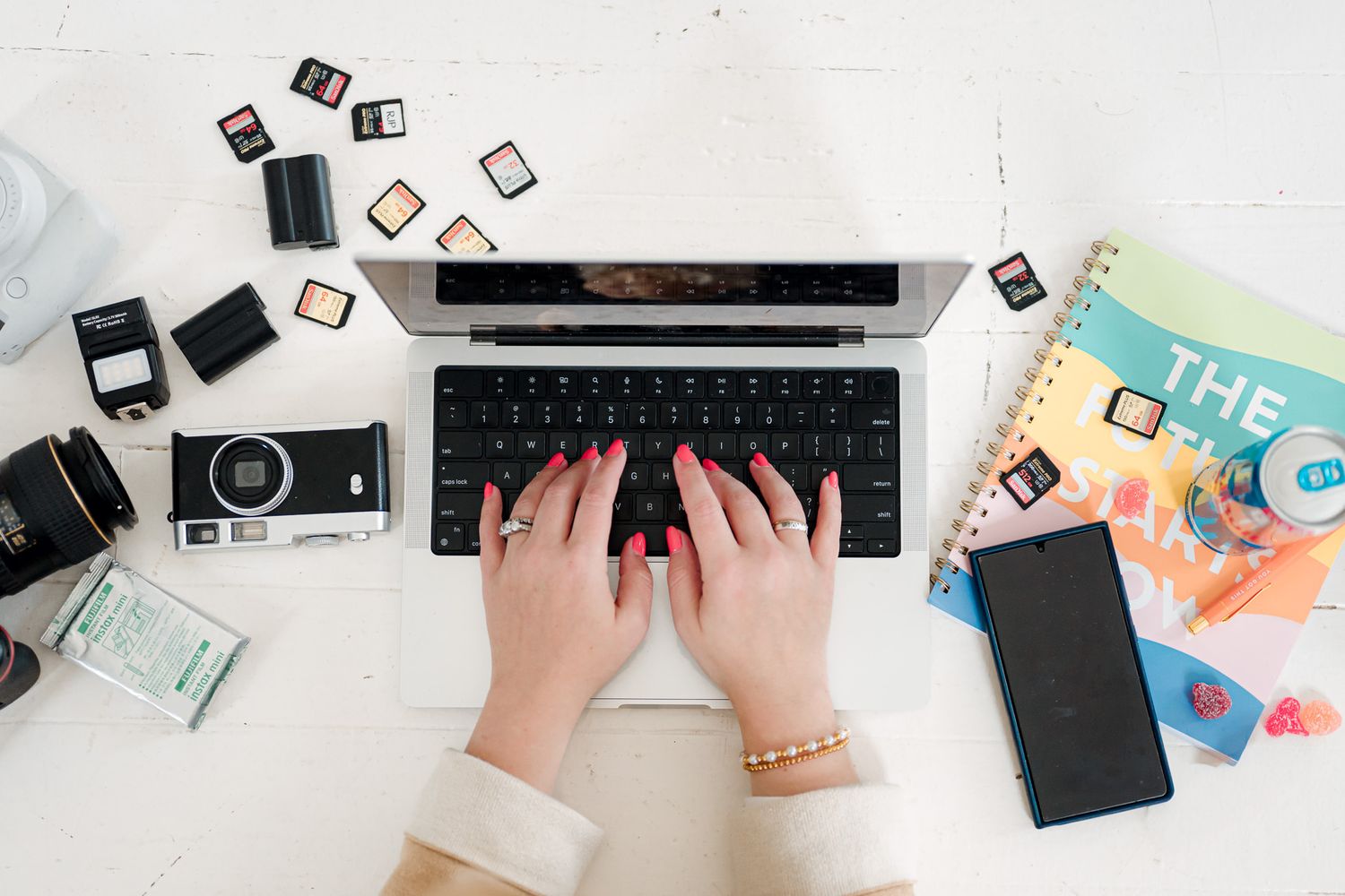 Hands typing on laptop keyboard with scattered SD memory cards and office supplies on white desk surface.
