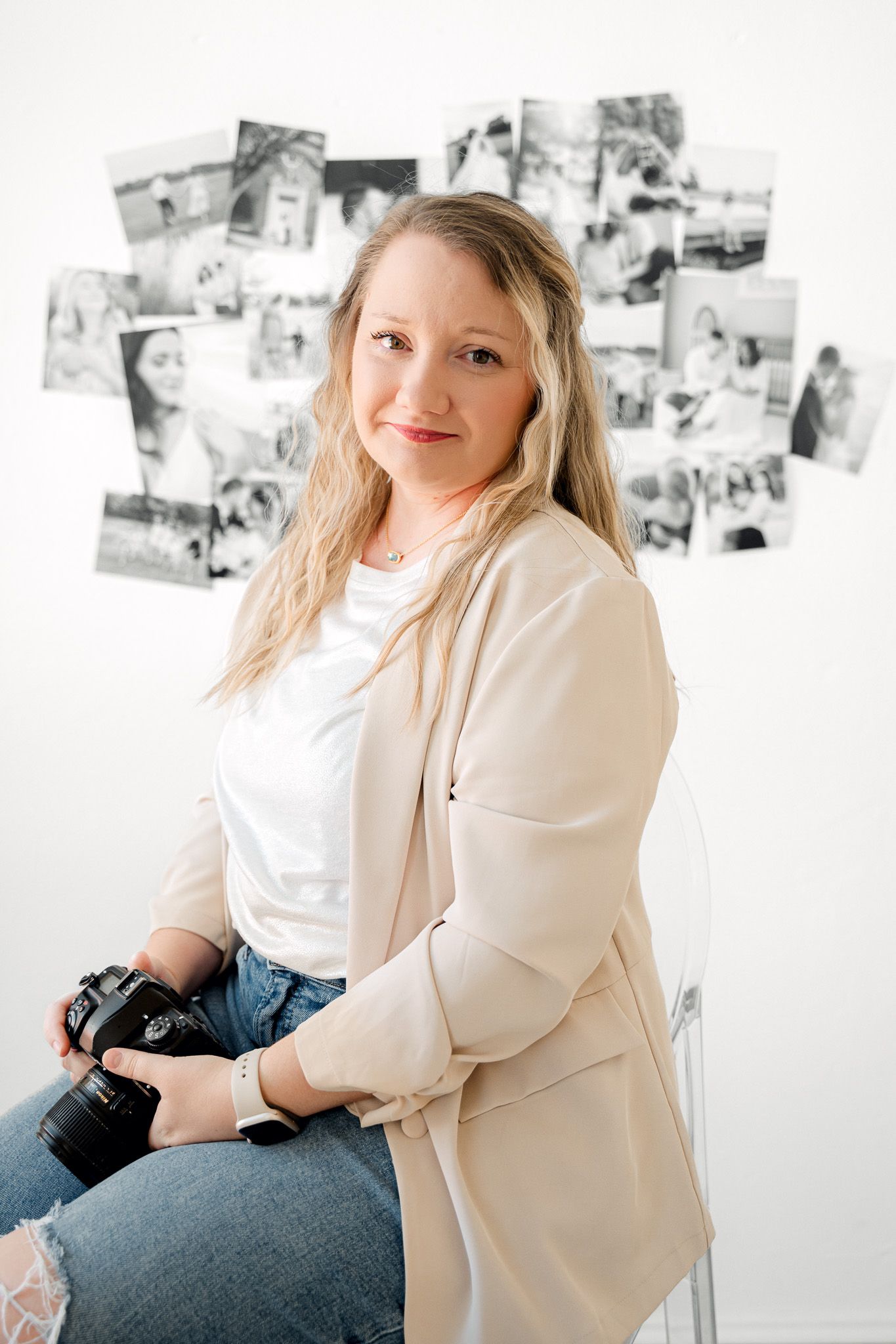 Professional photographer sits with camera in white studio space with photo wall gallery.