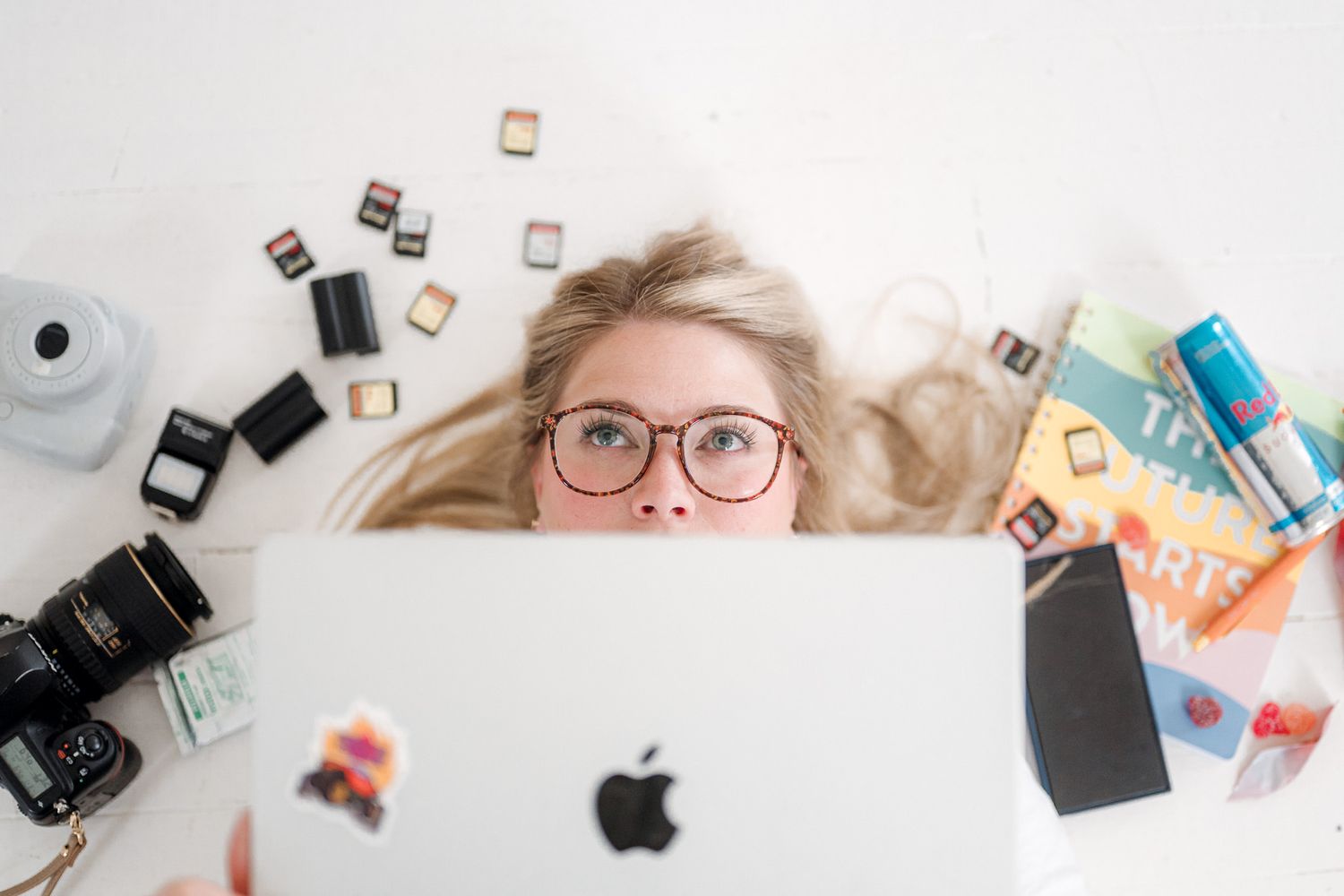Flatlay of tech gadgets and accessories including Apple products, camera gear, and office supplies on white background.
