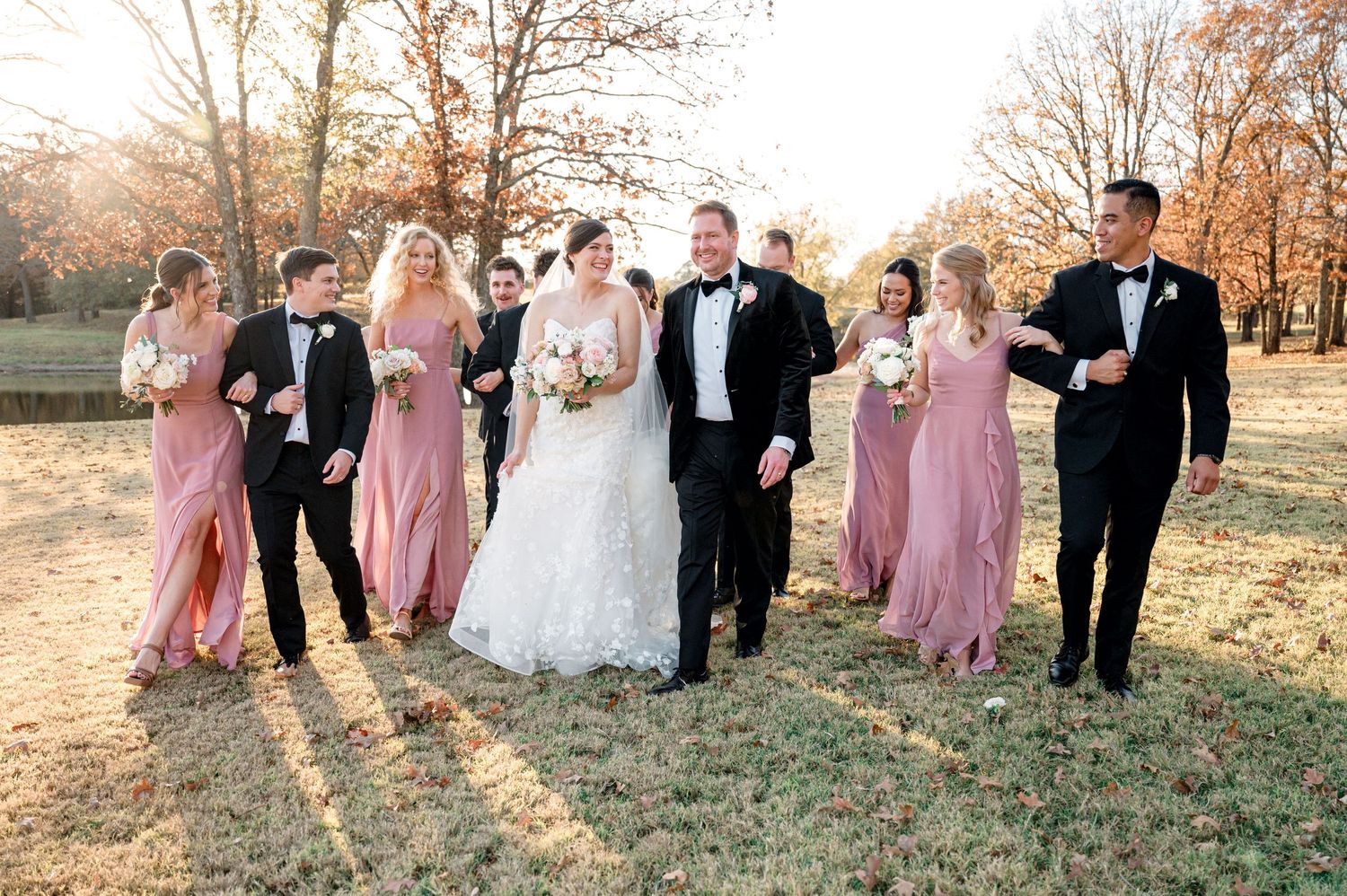 Wedding party in pink bridesmaid dresses poses together during golden hour.