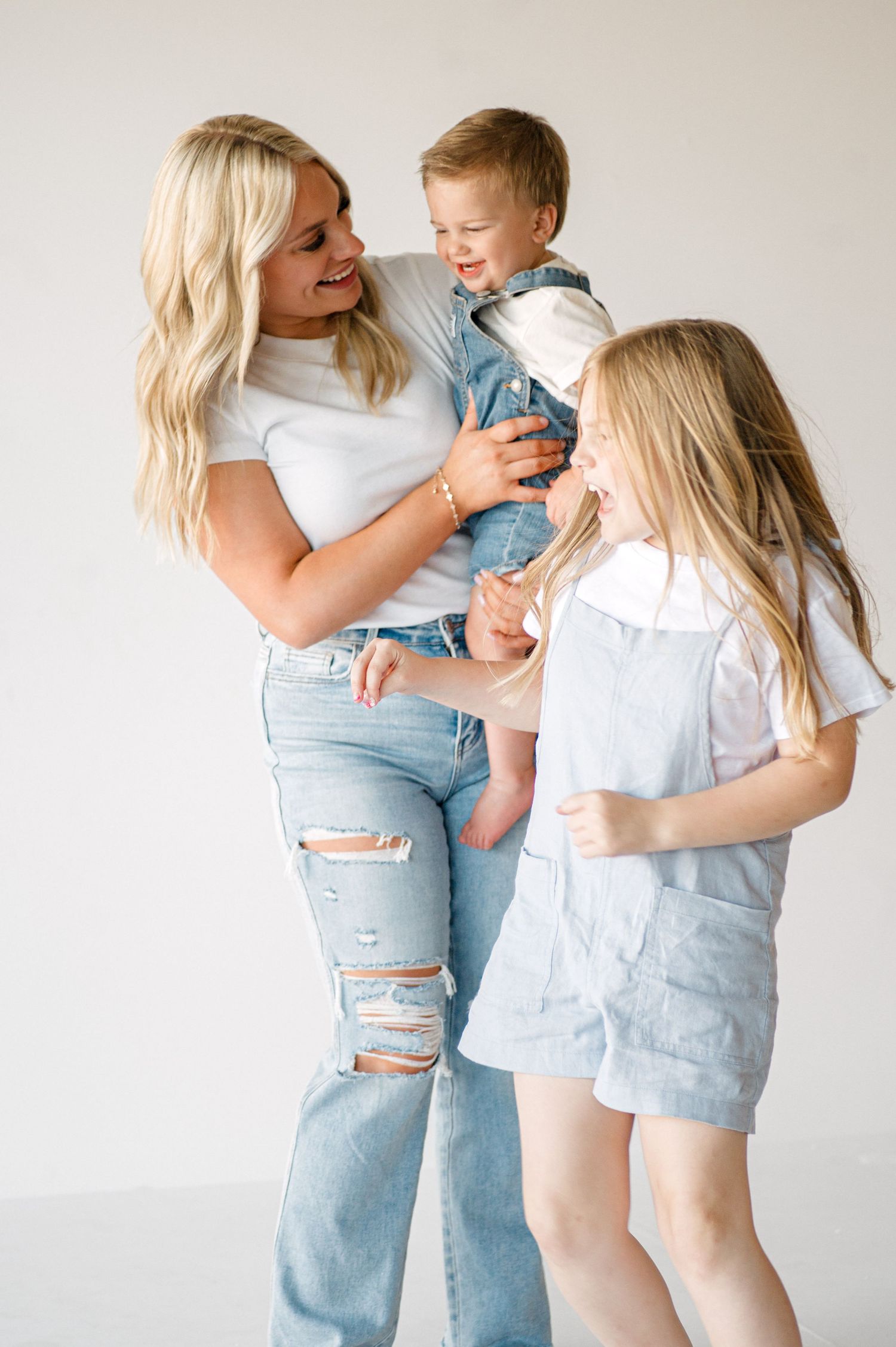 Family wearing white shirts and light denim embrace and laugh together against white background in lifestyle photoshoot.