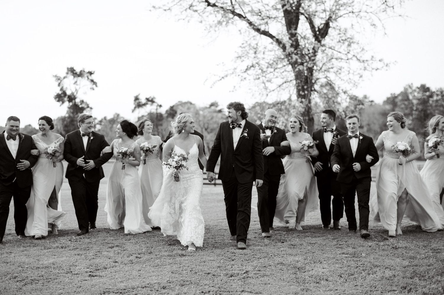 Wedding party members in formal attire walk together in a line across an outdoor setting.  Wedding Photographer tyler tx