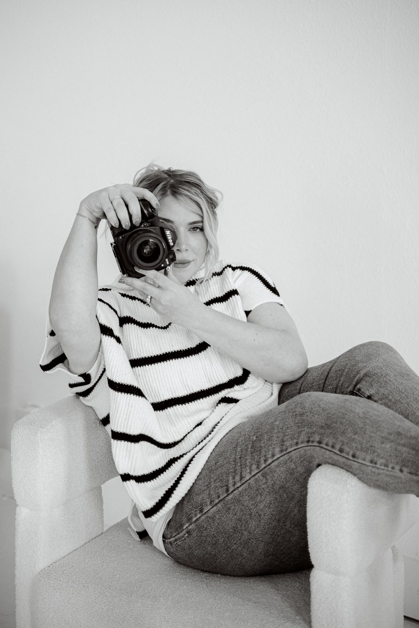 Black and white photo series of someone lying on a couch in jeans and striped shirt taking photos with a camera.