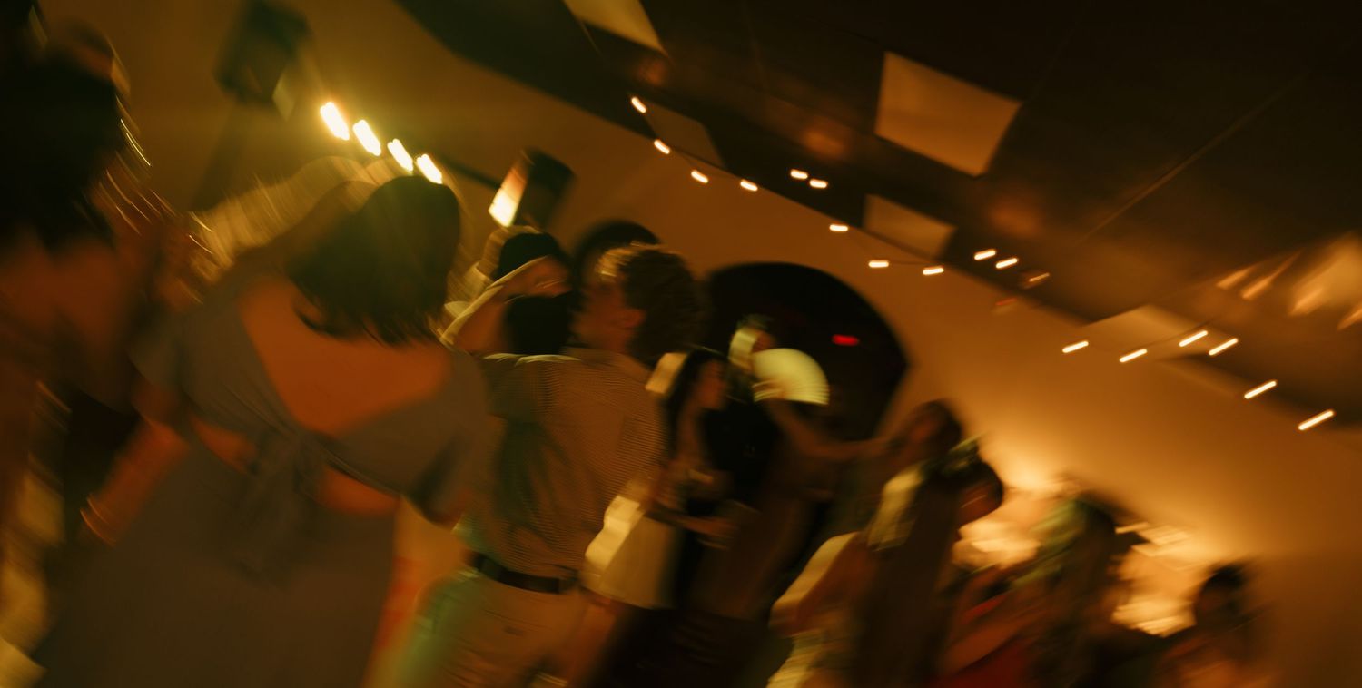 Blurry motion shot of people dancing at a dimly lit nightclub with warm orange and yellow lights.