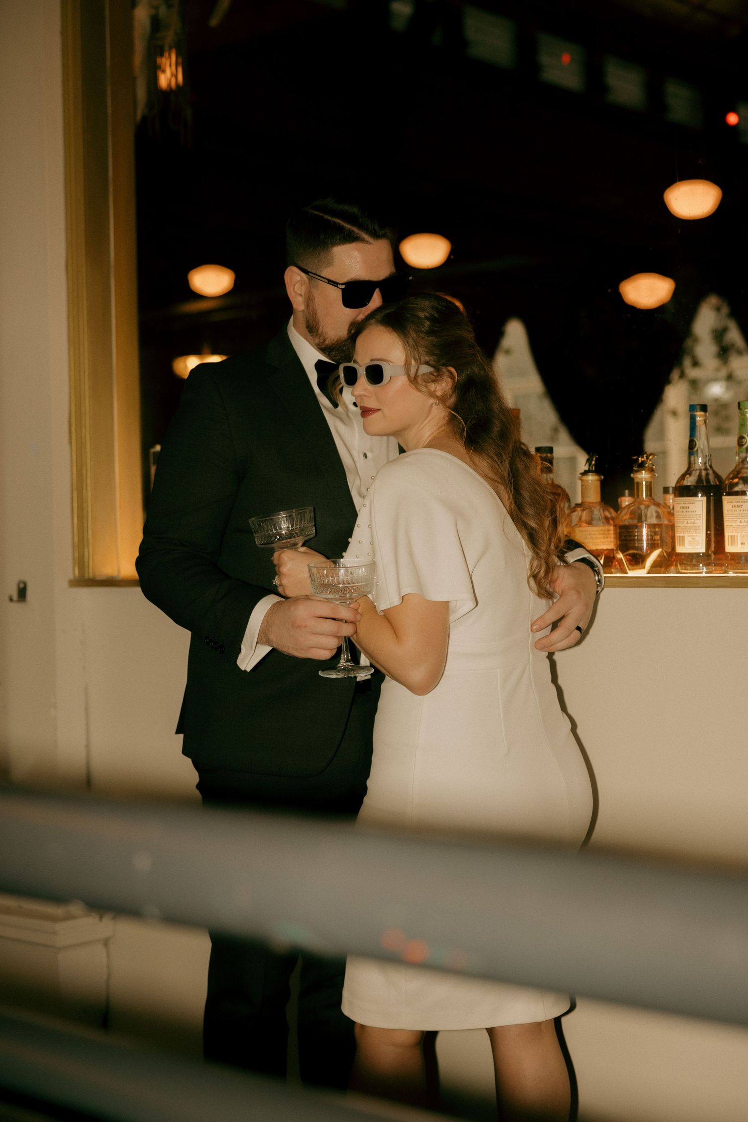 Couple dancing together at a dimly lit wedding reception with warm glowing lights in the background.