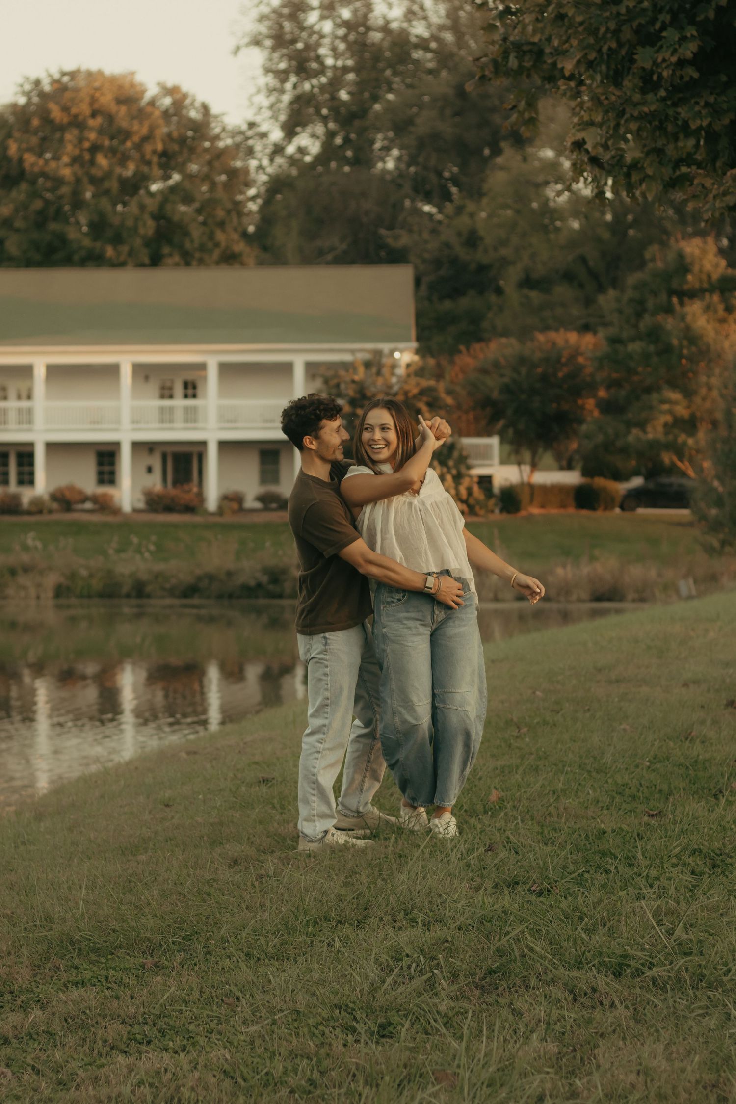 A couple shares a tender moment together on a grassy hill beside a tranquil pond during golden hour.
