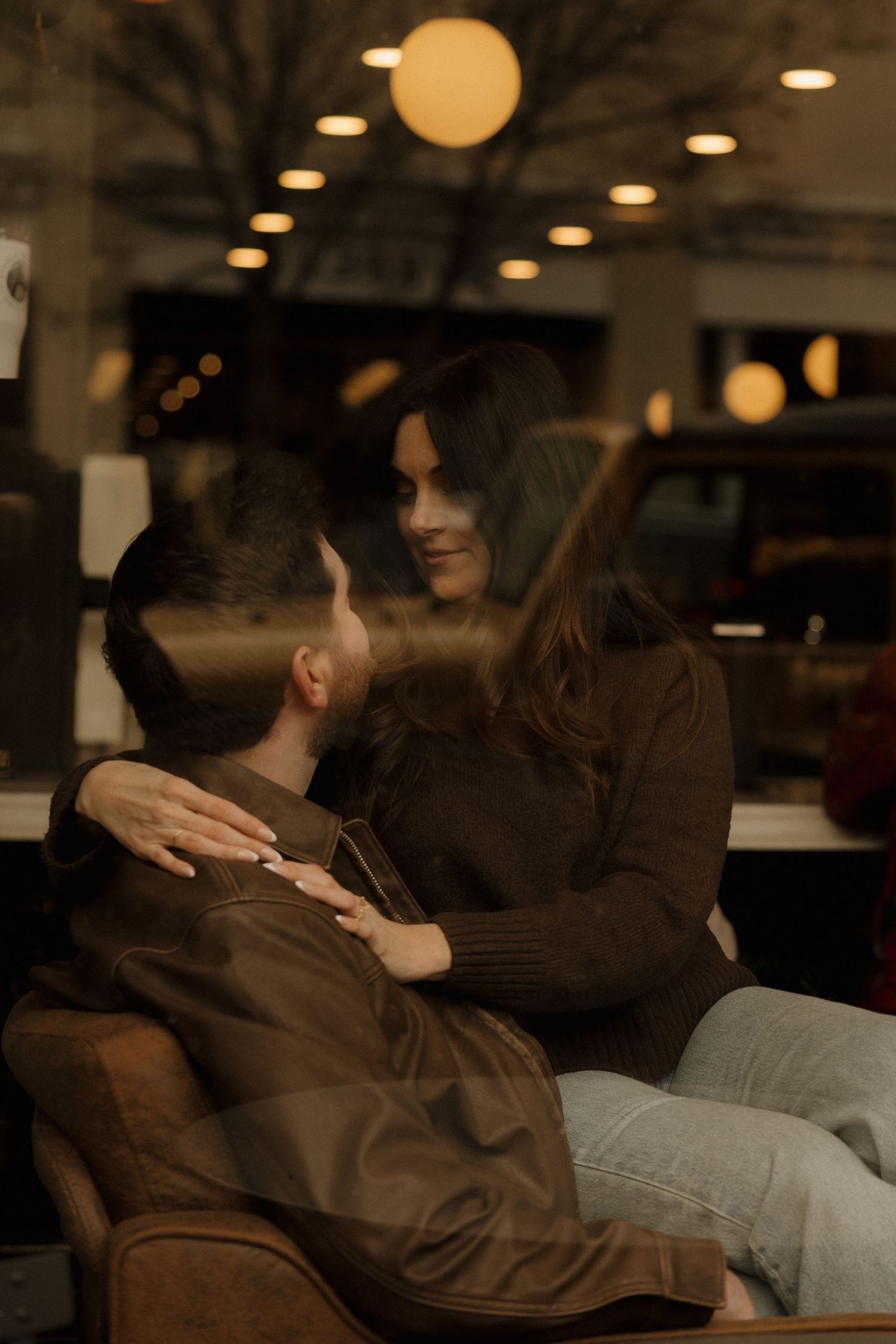 A couple shares an intimate moment on a couch in a dimly lit room with round pendant lights overhead.