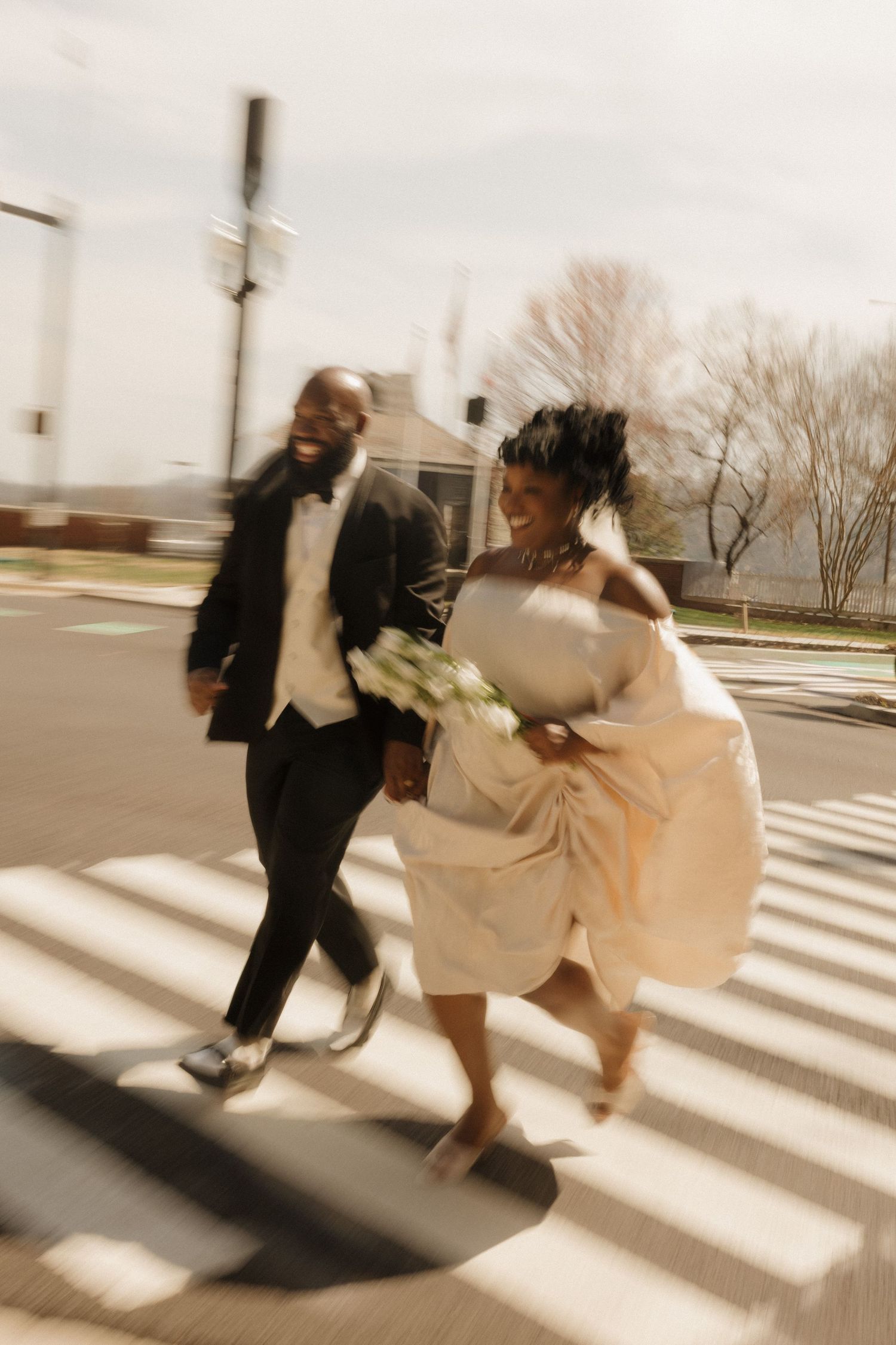 Two figures in contrasting black and cream outfits dance energetically across a sunlit crosswalk in a dynamic motion sequence.