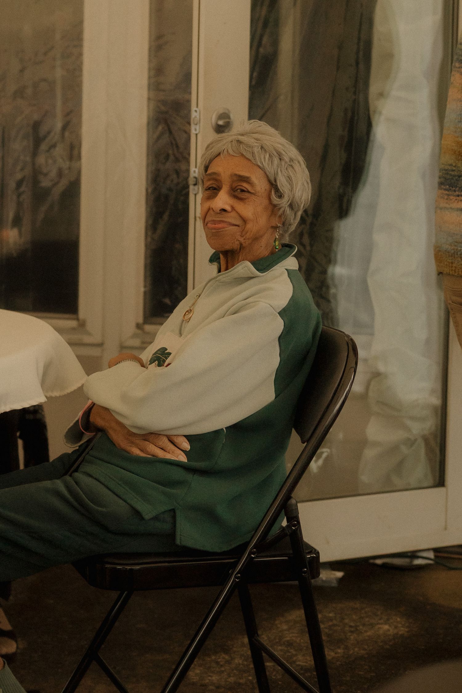 An elderly person in a green sweater sits comfortably in a folding chair while enjoying a relaxing moment outdoors.