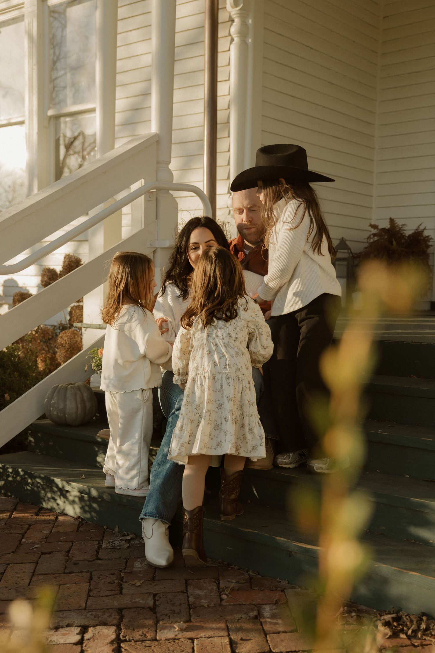 Children in white dresses gather on a brick porch during golden hour.