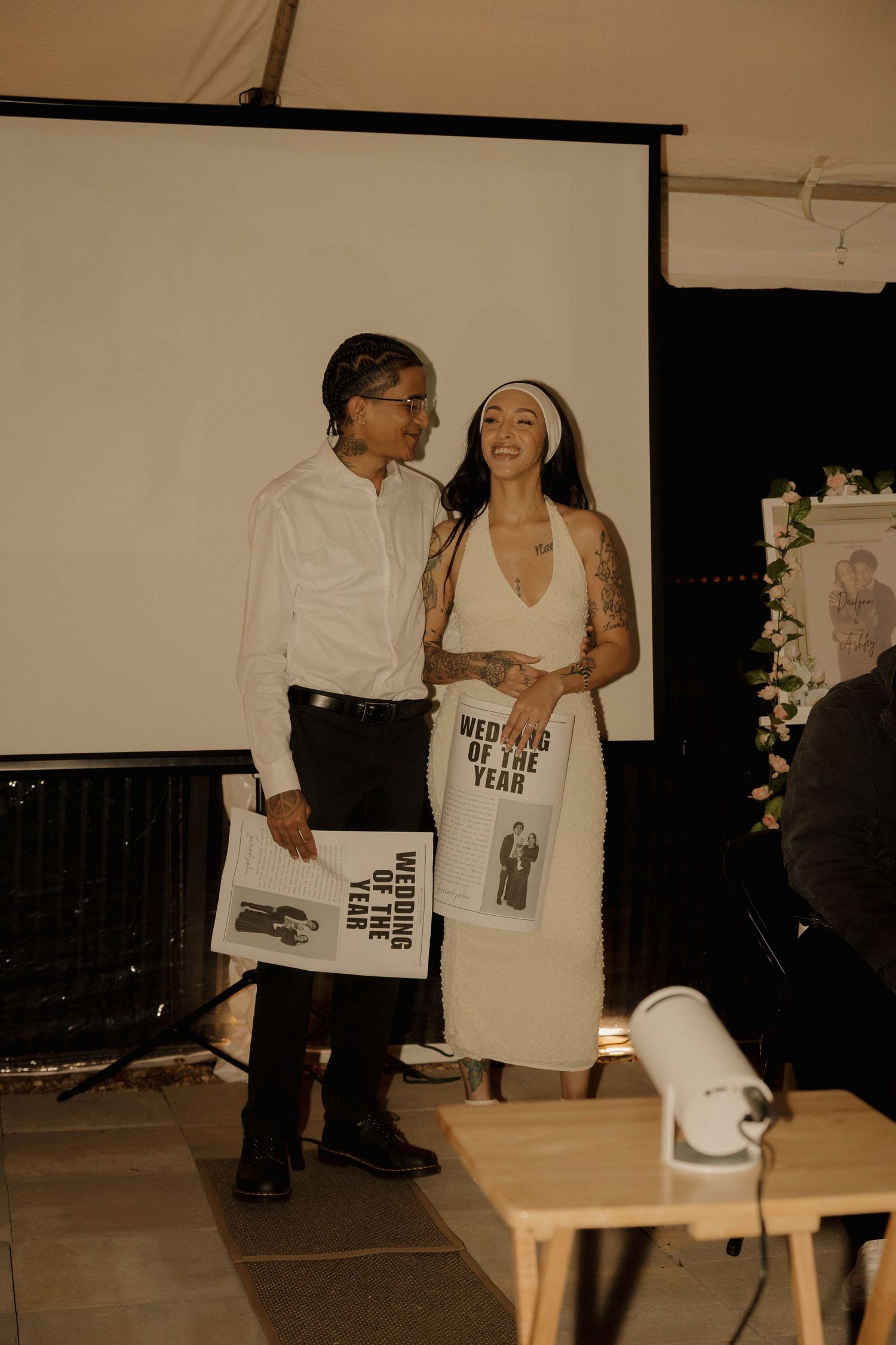 Two people stand together on stage sharing a laugh while holding promotional materials at an event presentation.