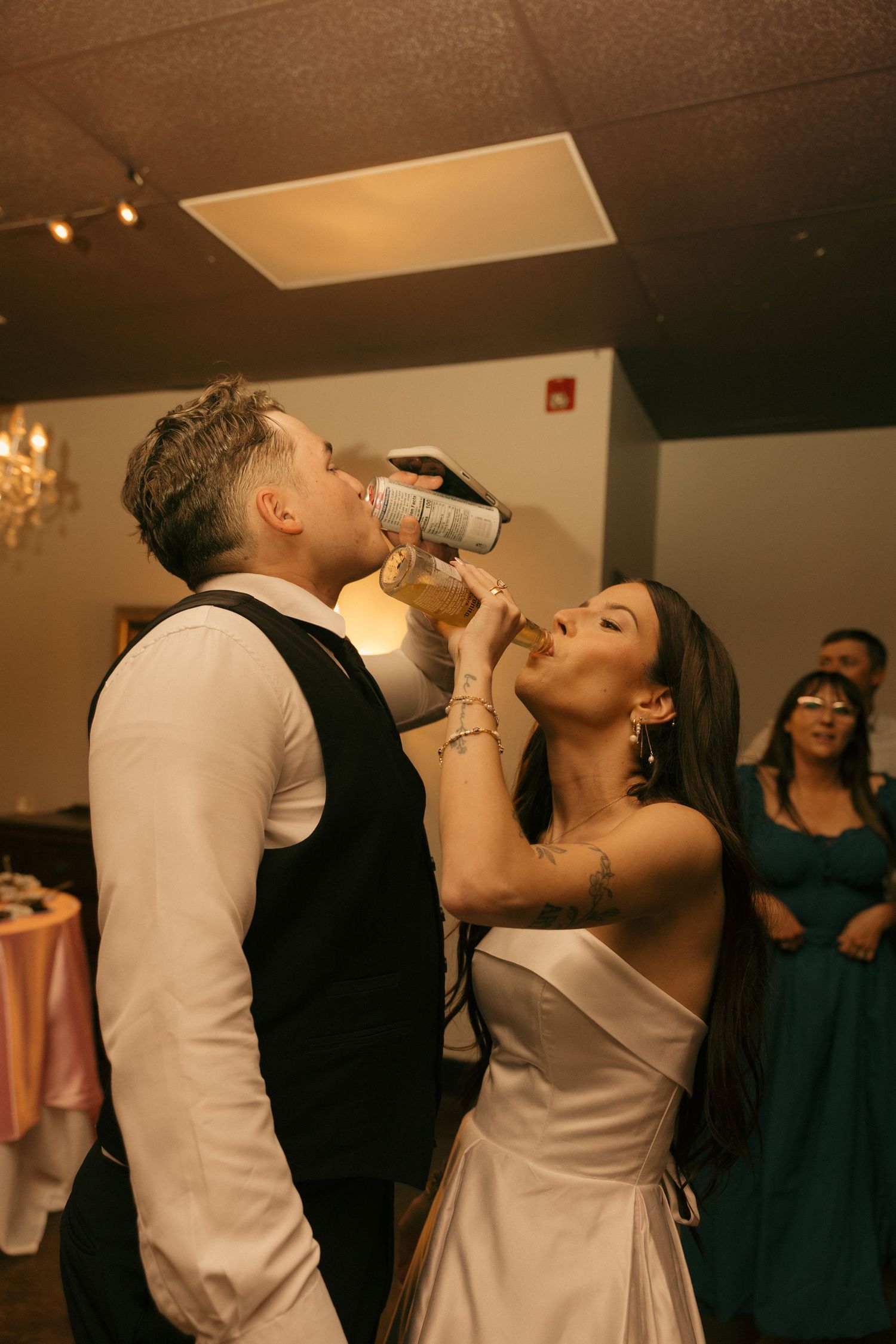 Bride and groom sharing a drink from a bottle at their wedding reception celebration.