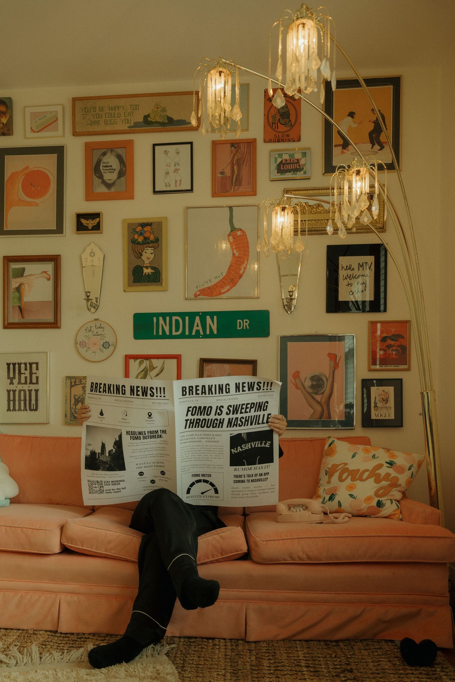 A pink couch against a wall decorated with framed artwork and hanging lights creates a cozy vintage atmosphere.