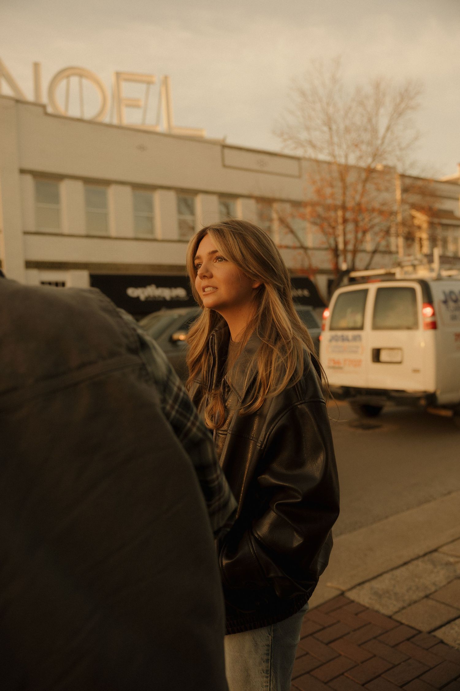 A series of sepia-toned photos showing a person in a leather jacket standing against an urban backdrop in moody lighting.