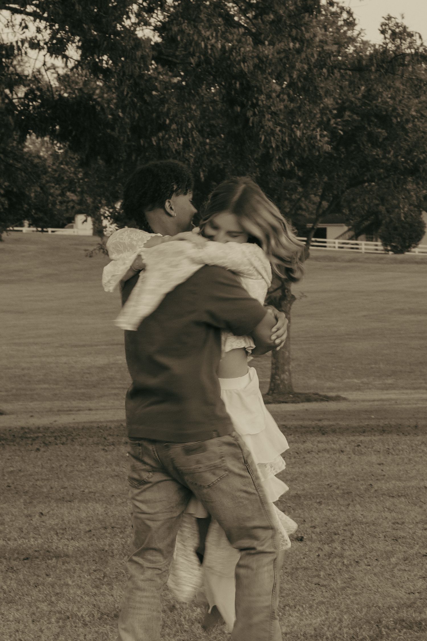 A sequence of sepia-toned photos showing two people hugging and spinning in a grassy field under trees.