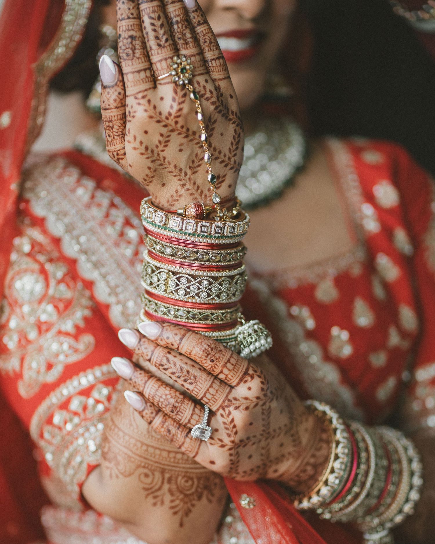 Indian bride showcasing intricate henna mehndi designs on hands, wearing red and gold bangles and bridal lehenga.
