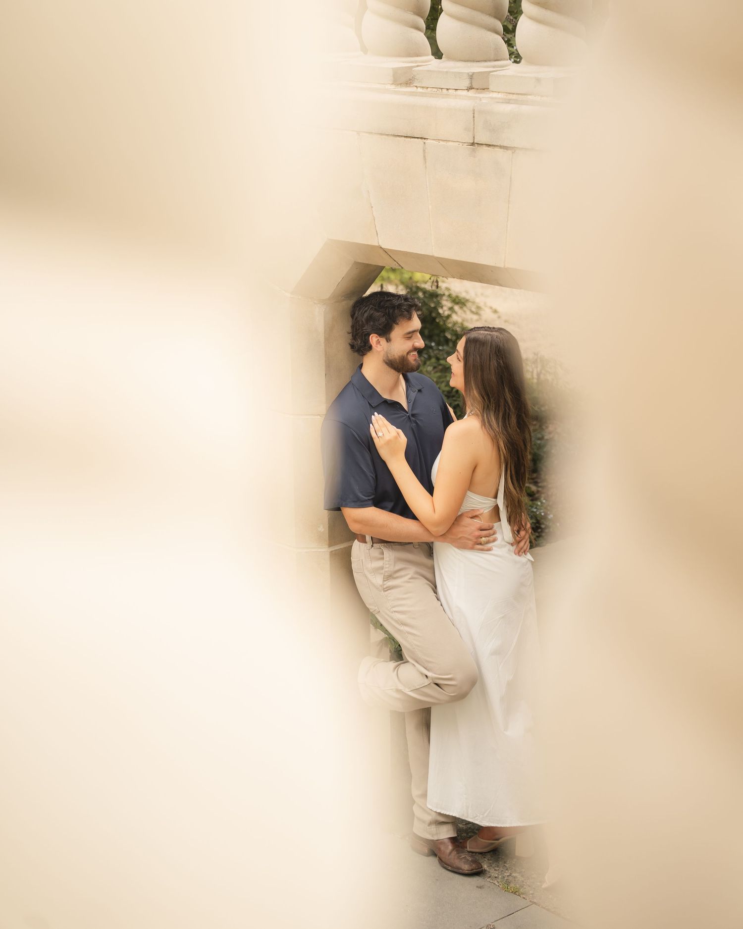 Couple sharing a romantic moment framed by stone archway, man in navy shirt, woman in white dress.