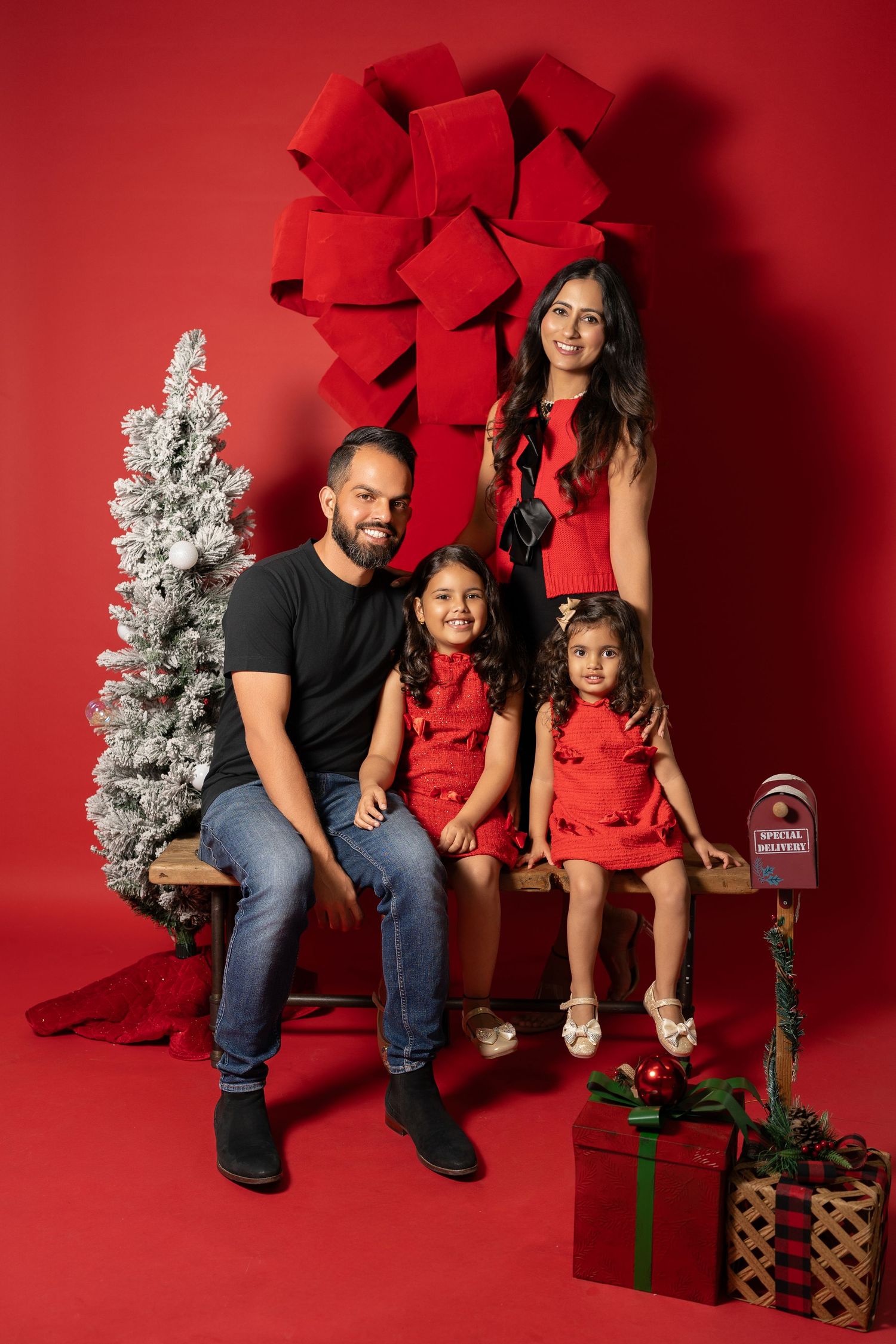 Holiday portrait with family in red and black outfits seated with Christmas decorations on red background.