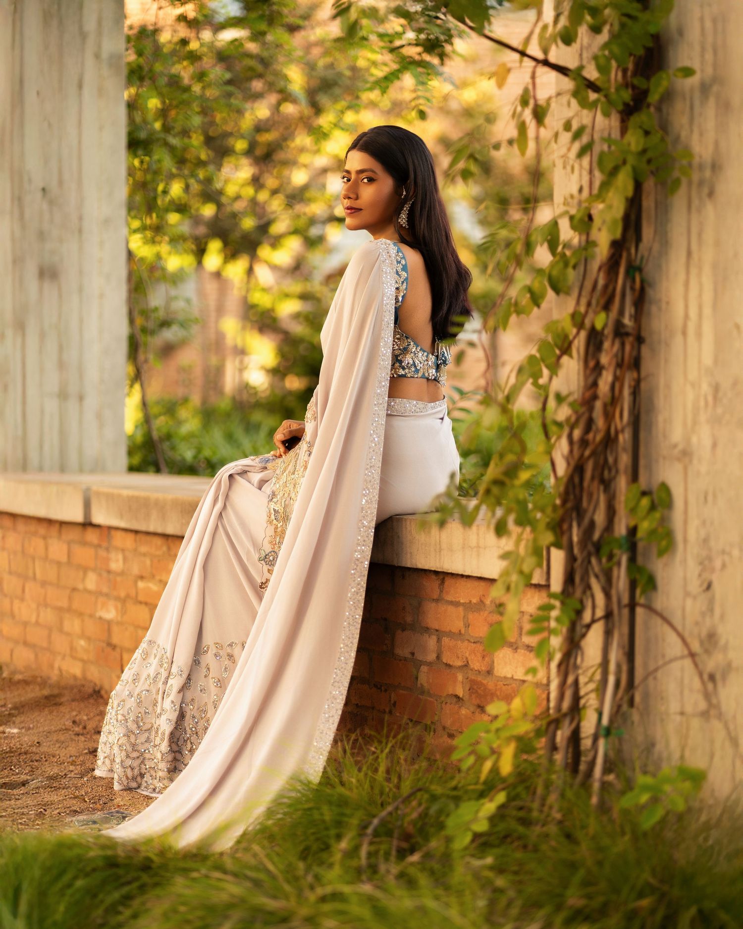 An elegant outdoor photoshoot featuring traditional Indian attire against a garden wall.