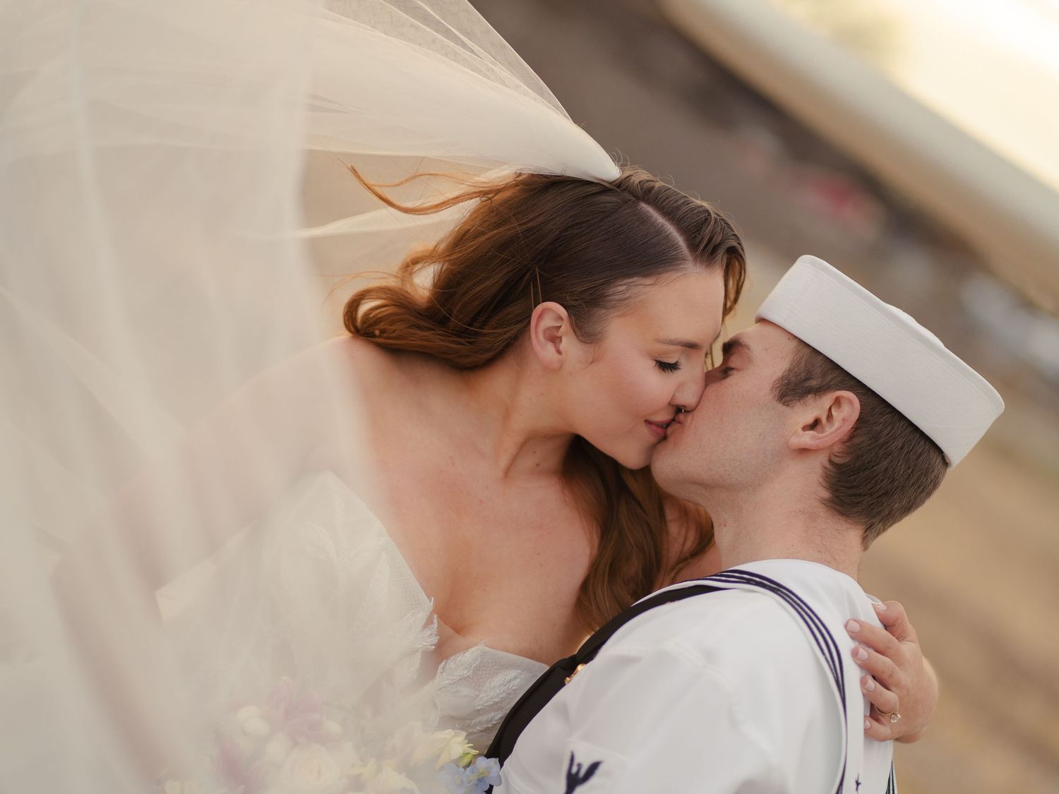 A couple in wedding attire share a tender kiss during their military wedding ceremony.