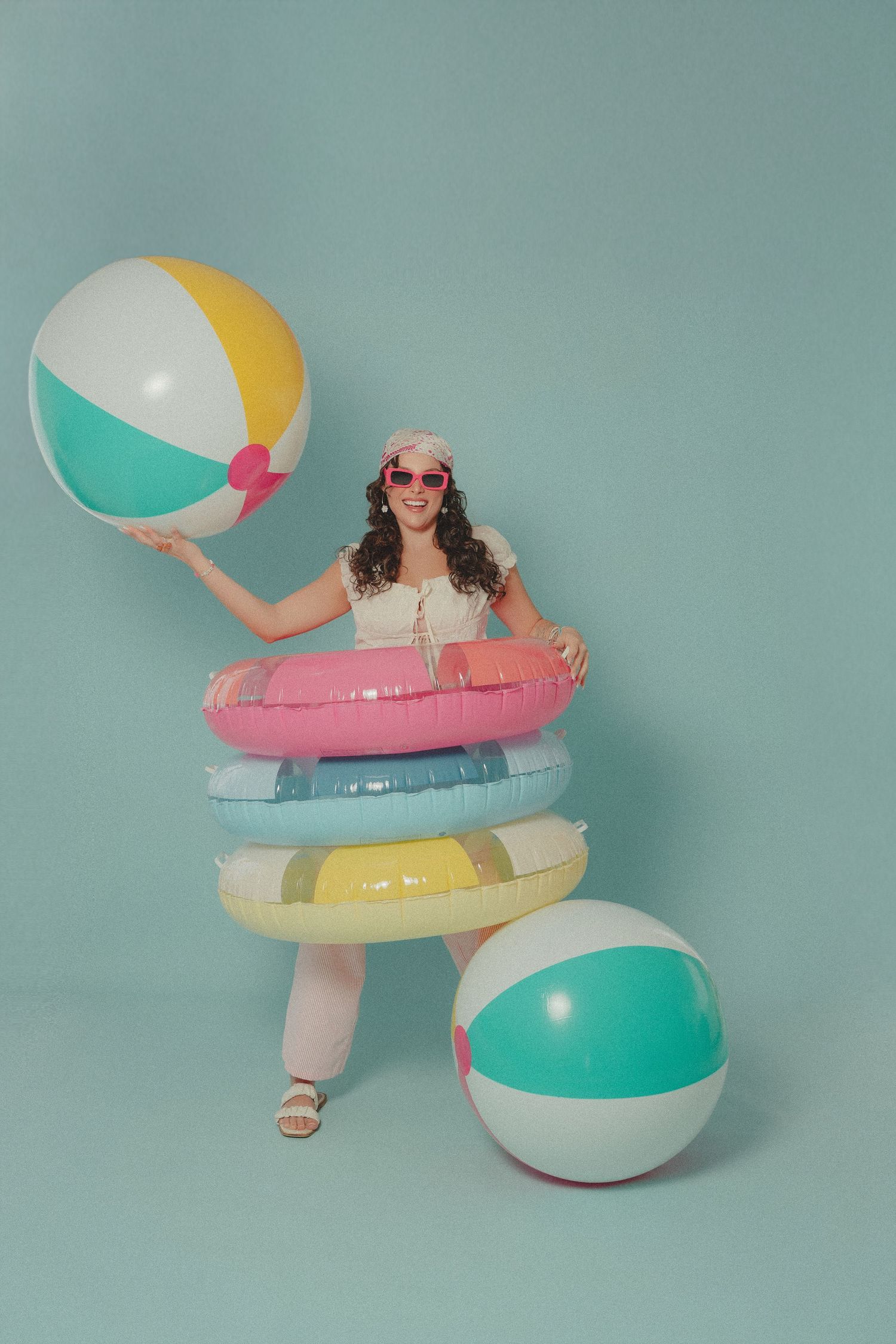 Cheerful woman in pink sunglasses holding beach balls with colorful inflatable rings on mint background.