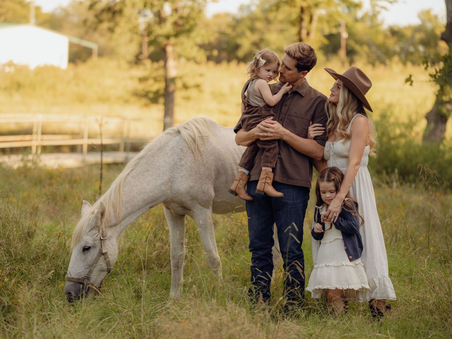 Family photoshoot in a rustic field setting with horses in the background.