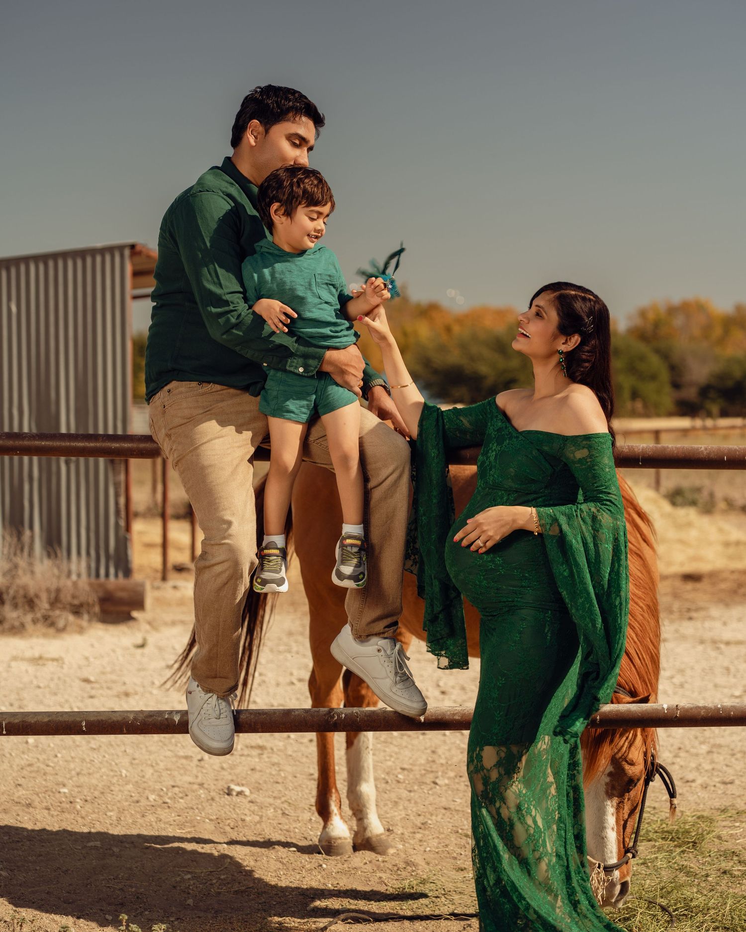 A family in matching green outfits poses with a horse at a ranch, with a pregnant woman in an elegant green gown.