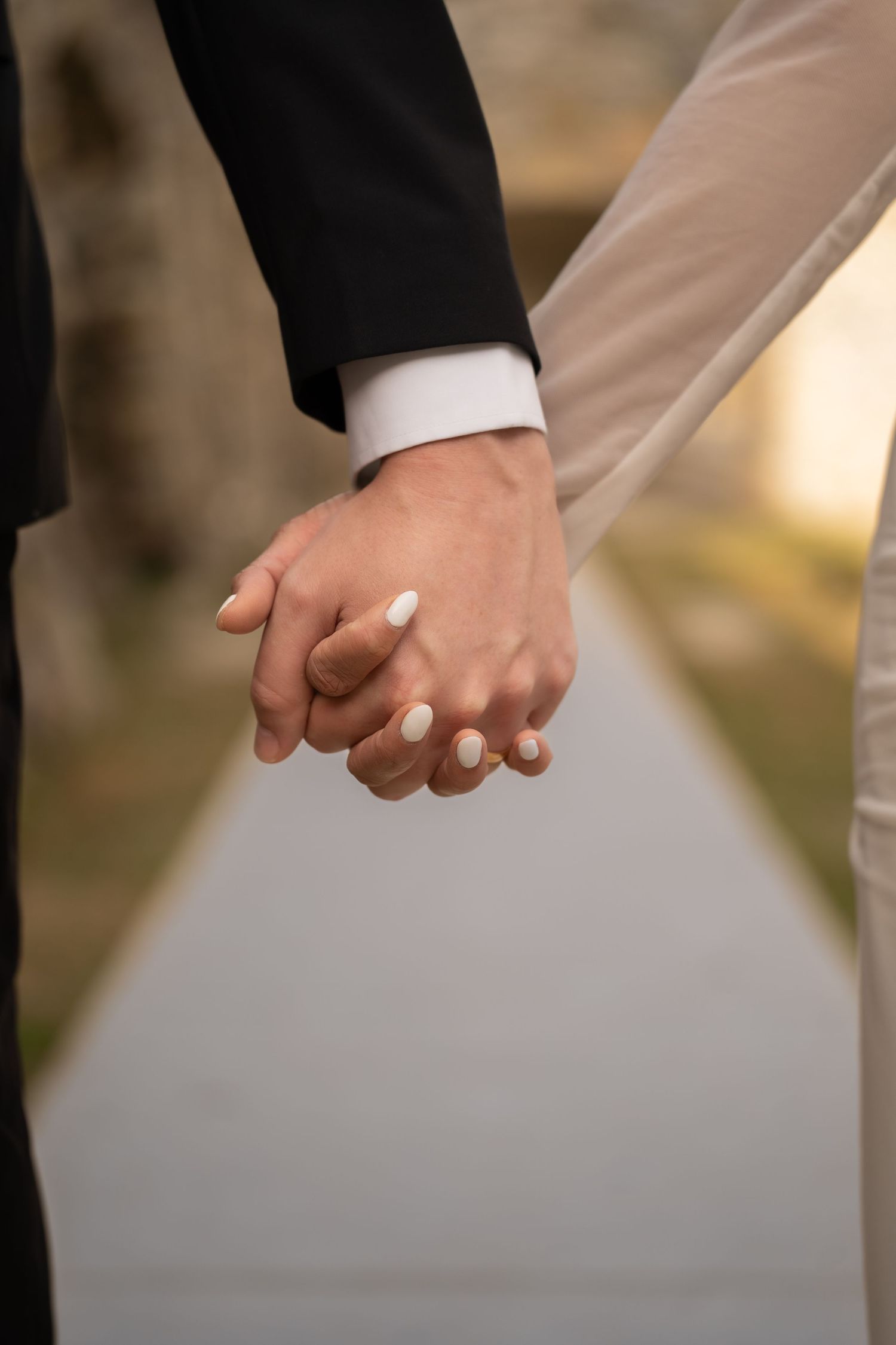 Close-up of newlyweds holding hands showing white manicured nails.