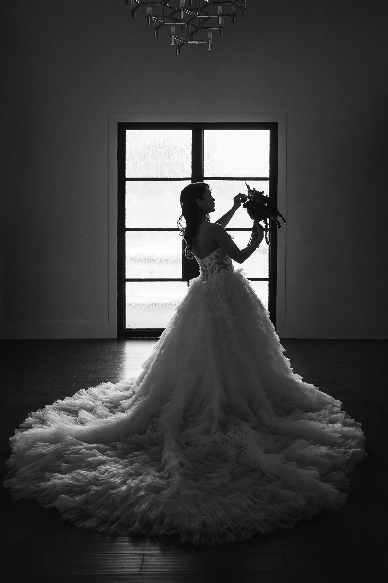 Dramatic silhouettes of a wedding dress against window light in black and white photography.