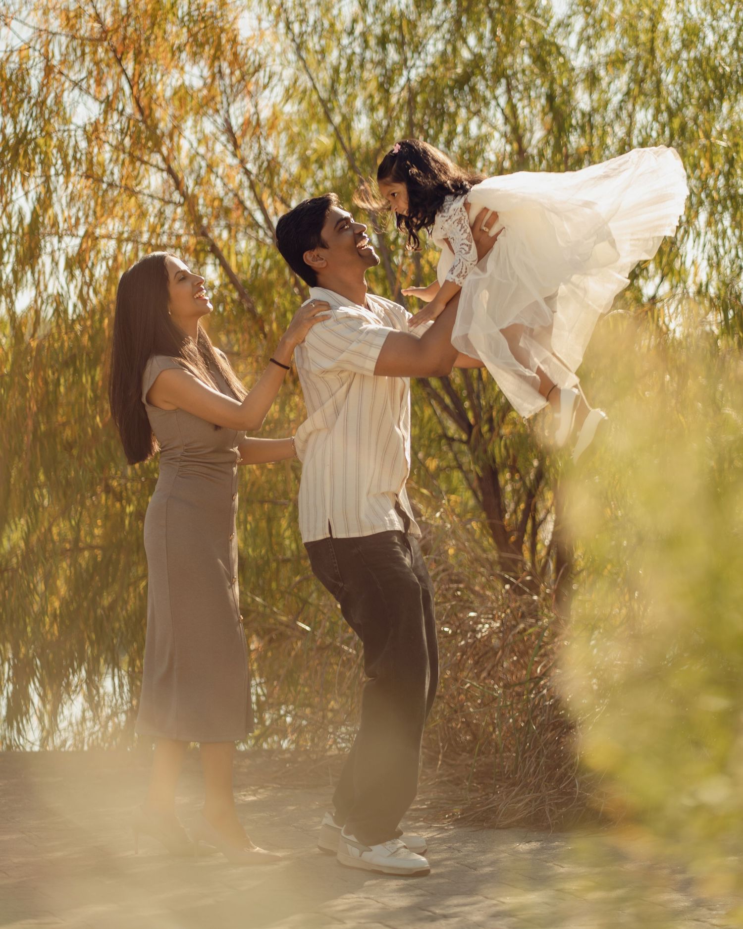 Couple dancing together in front of willow trees during a warm sunset.
