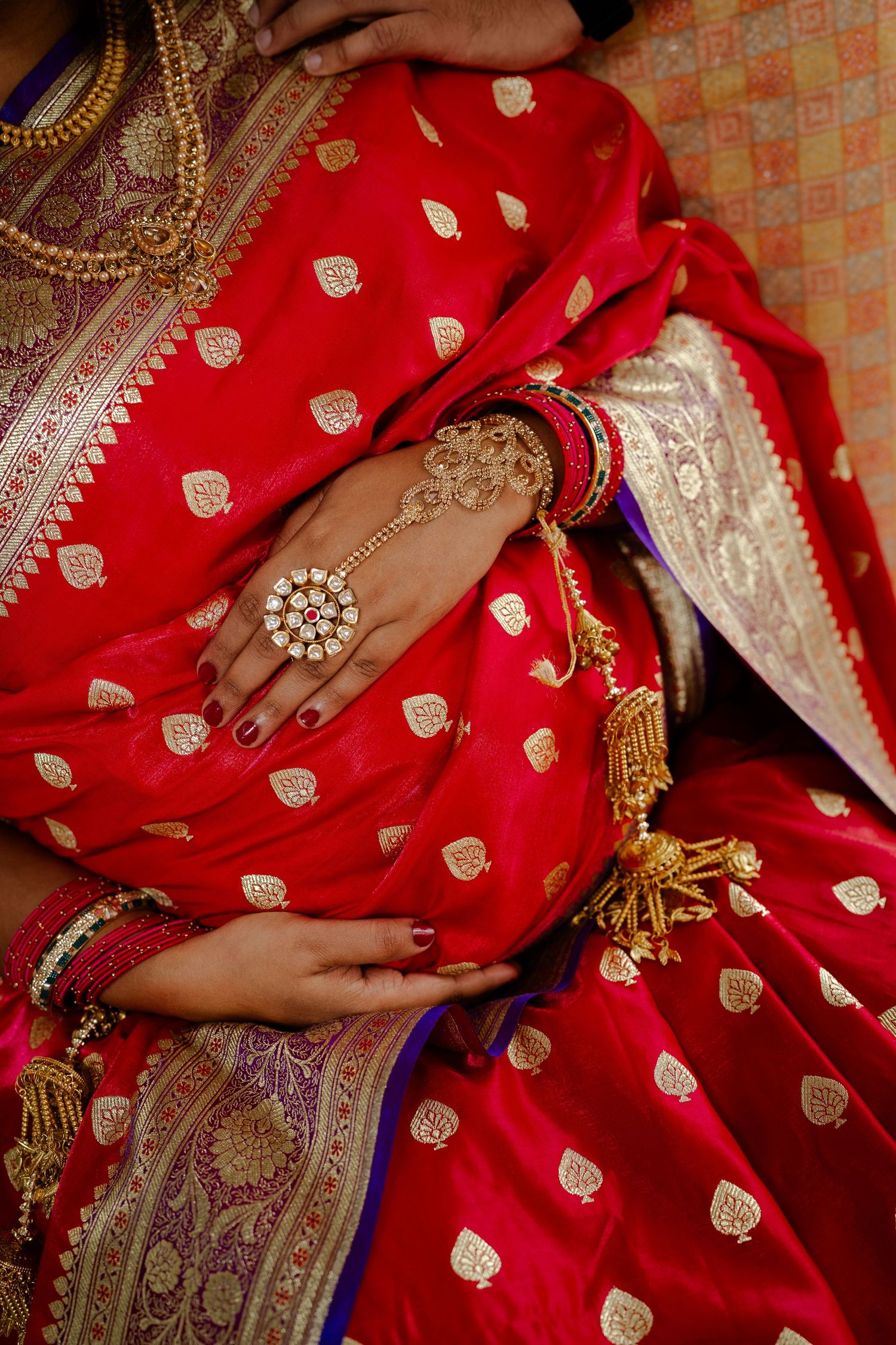 Indian bride in red and gold saree with intricate mehndi henna on hands and traditional gold jewelry and bangles.