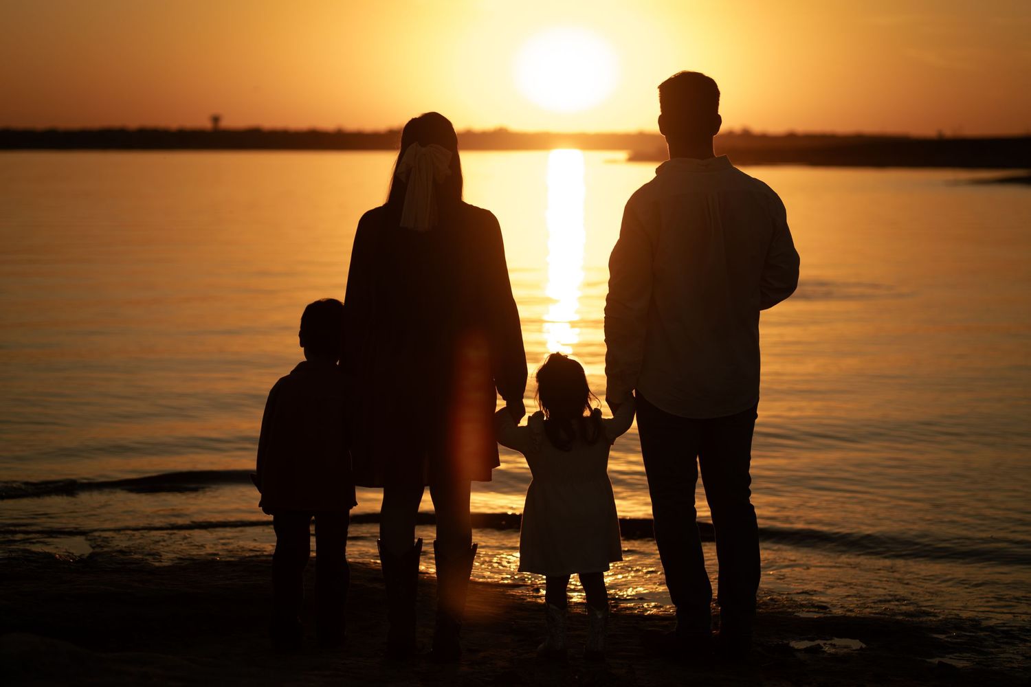Silhouettes of a group watching a vibrant orange sunset over calm waters.