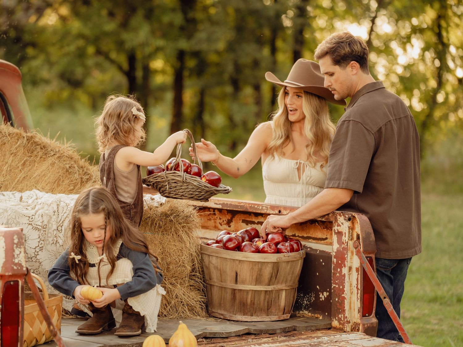 Family gathering around rustic wooden baskets and hay bales during autumn photoshoot.