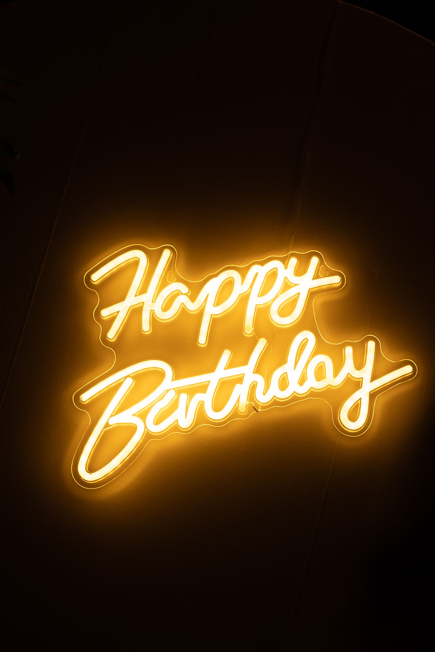 Glowing yellow neon sign displaying the words 'Happy Birthday' against a dark background.