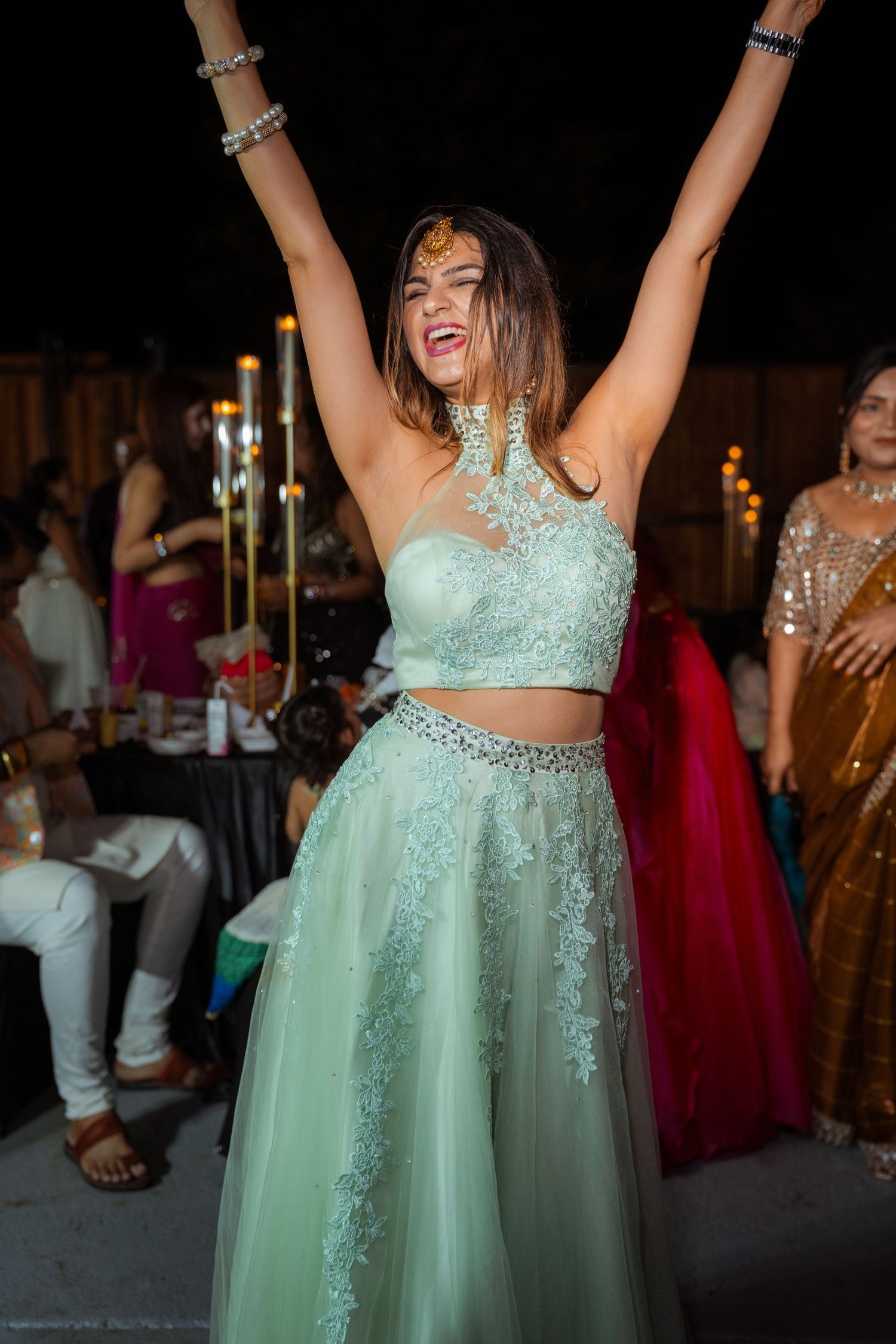 Person in mint green sparkly two-piece formal dress dances joyfully at an evening celebration.