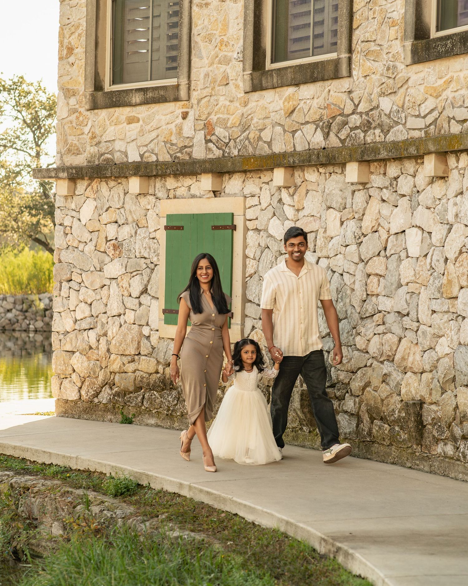 Family walking together along a stone building exterior with green shuttered windows during golden hour.