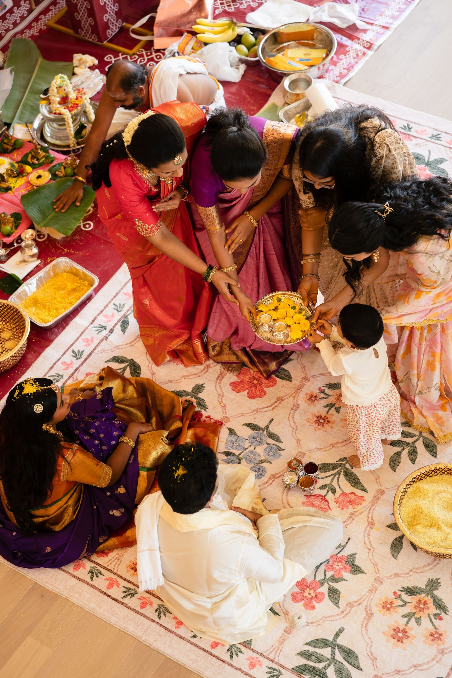 Aerial view of Indian family in traditional attire gathered around offerings during a Hindu ceremony.