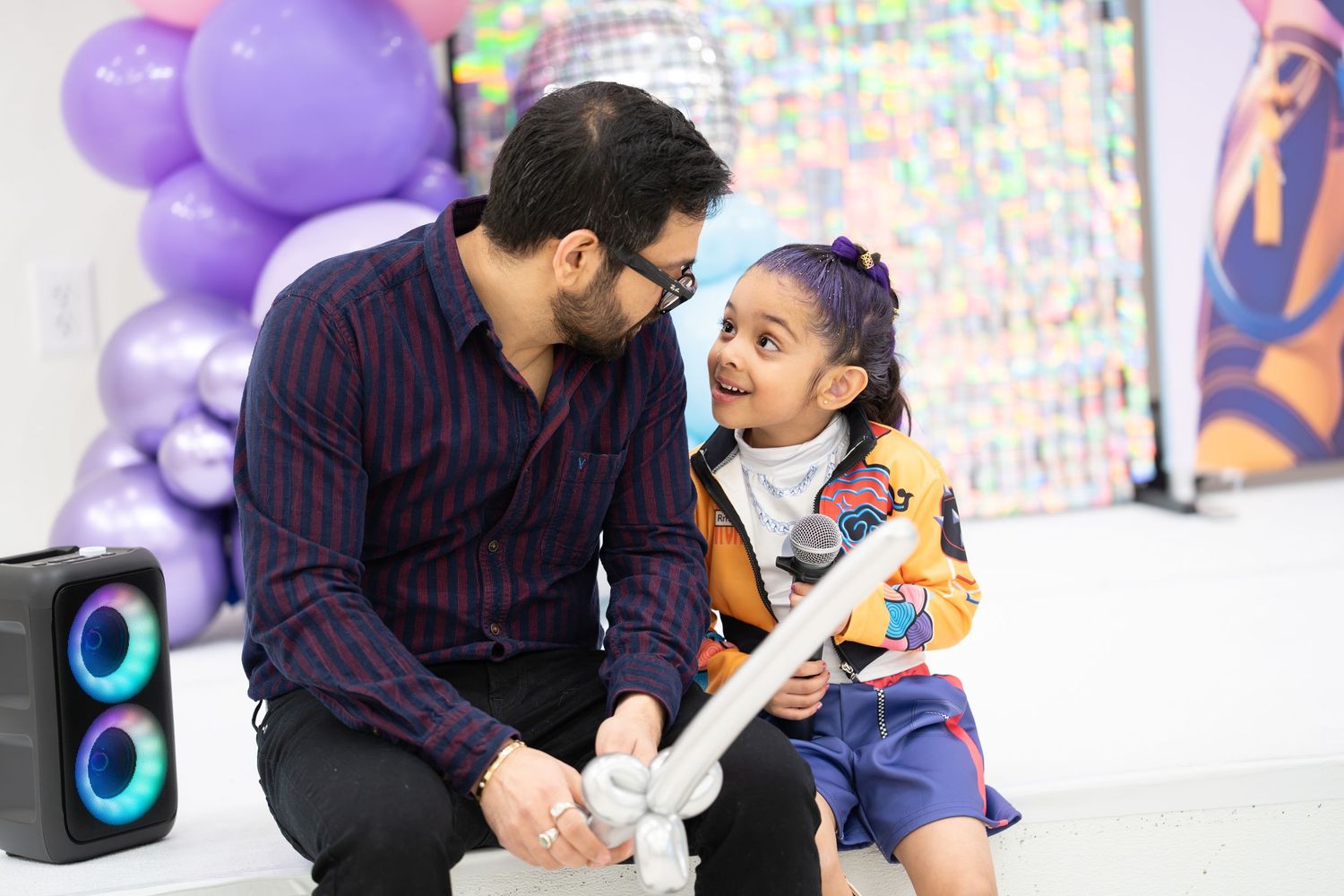 Parent and child share a joyful moment while playing music together with purple balloons in the background.