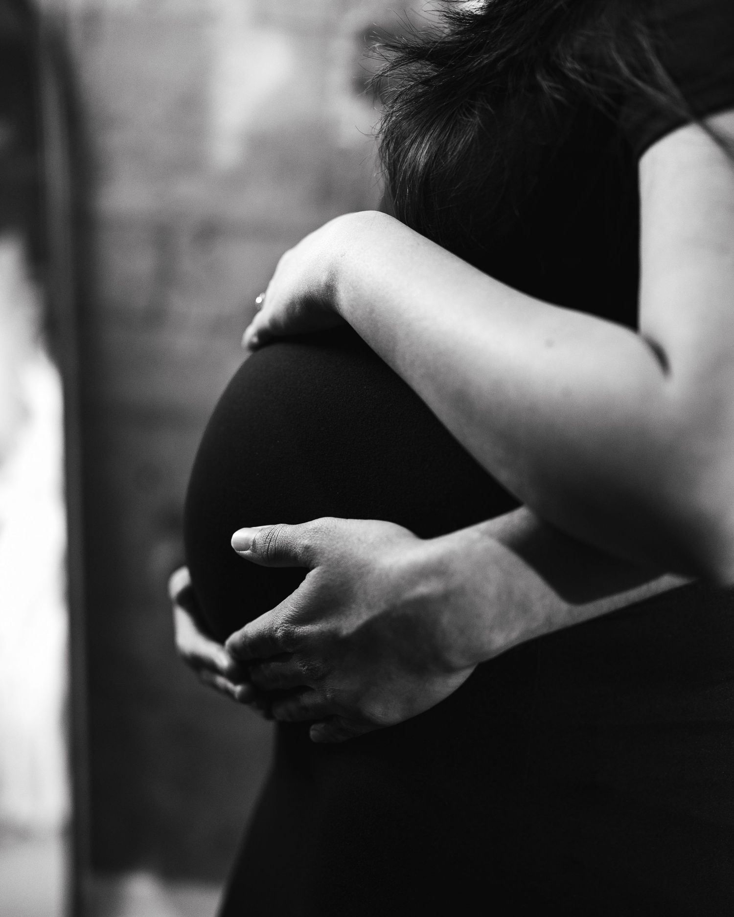 Black and white photo of a pregnant woman cradling her baby bump, wearing a black dress.