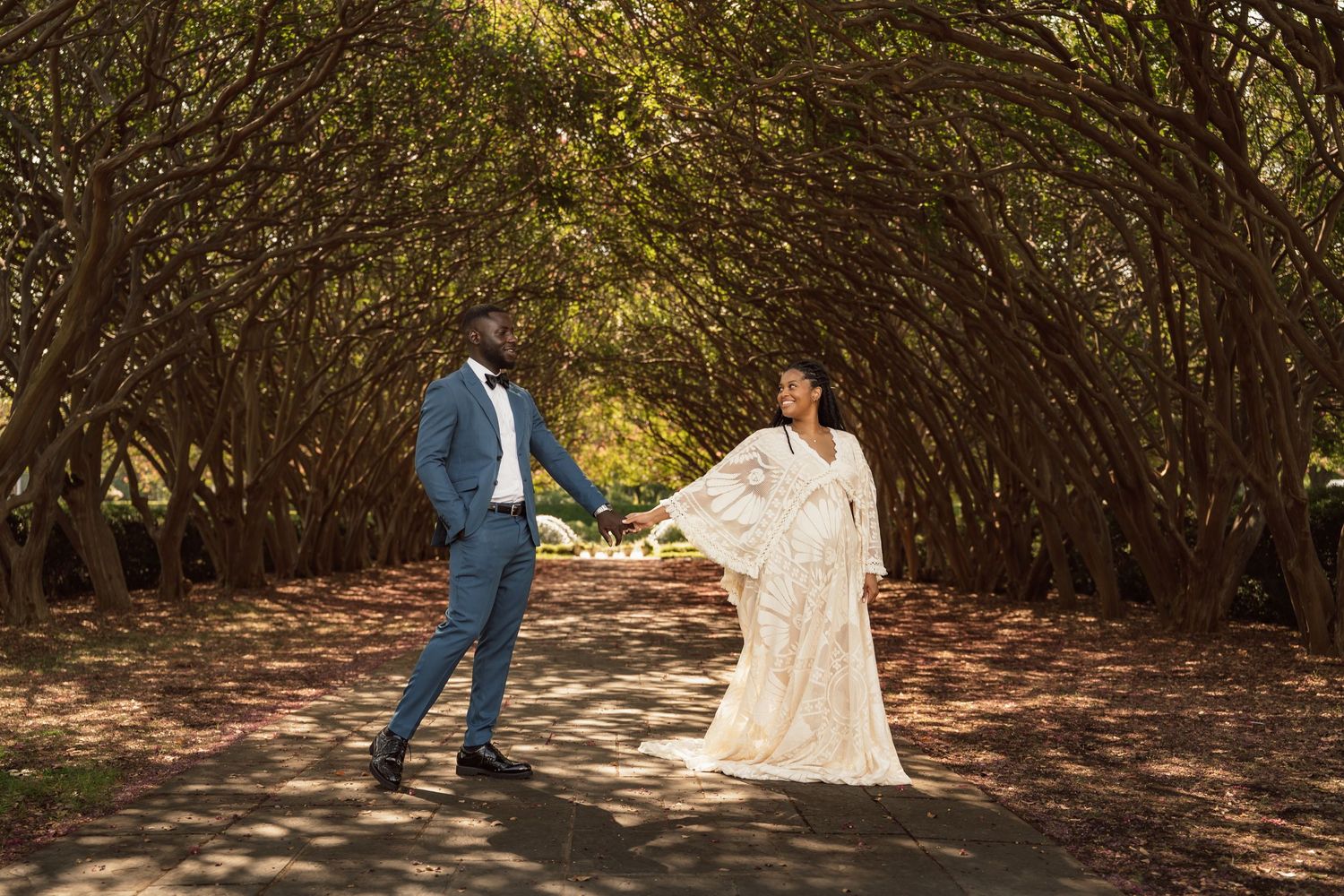Bride and groom hold hands under a stunning tree canopy tunnel on their wedding day.